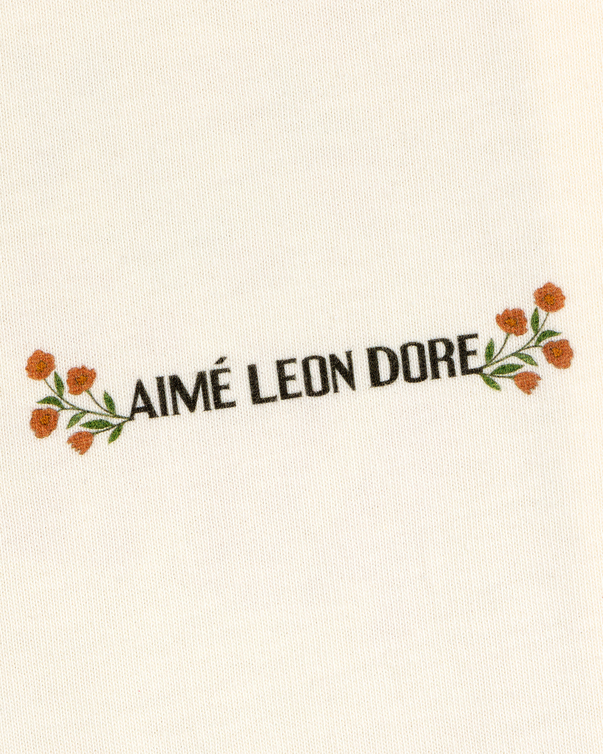 White Aimé Postcard Tee featuring black AIMÉ LEON DORE text, with orange flowers and green leaves.