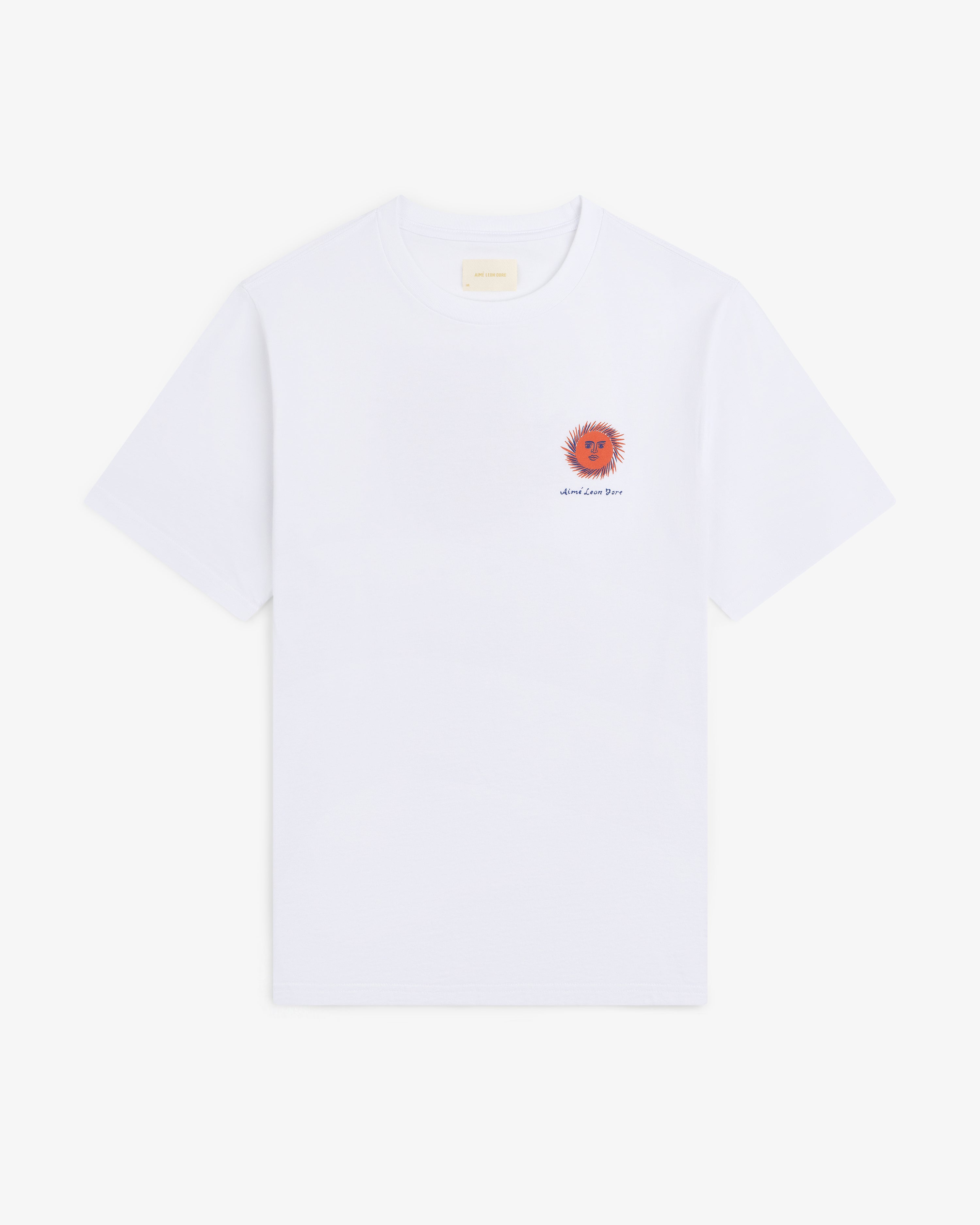 Fassianos "Sovereign Sun" Tee: white shirt with small orange sun and text on left chest, shown on plain background.
