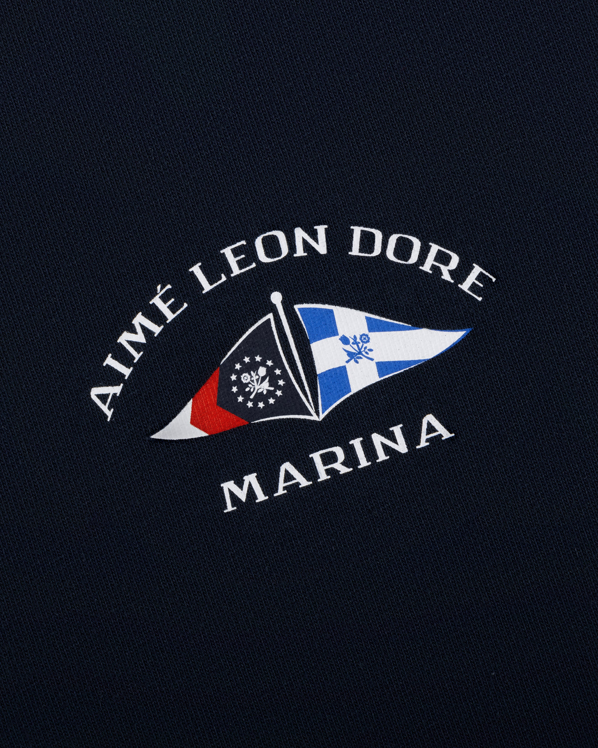 Navy Marina Tee featuring AIMÉ LEON DORE MARINA text and two nautical flags in the center.