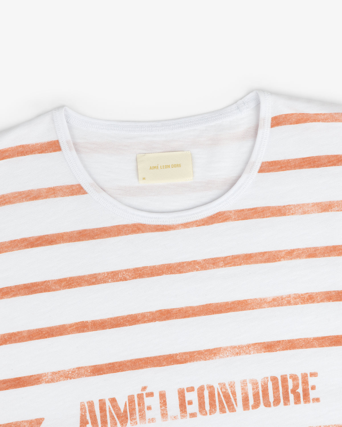 Slub Beach Tee: White t-shirt with orange stripes and AIMÉ LEON DORE printed on the chest.