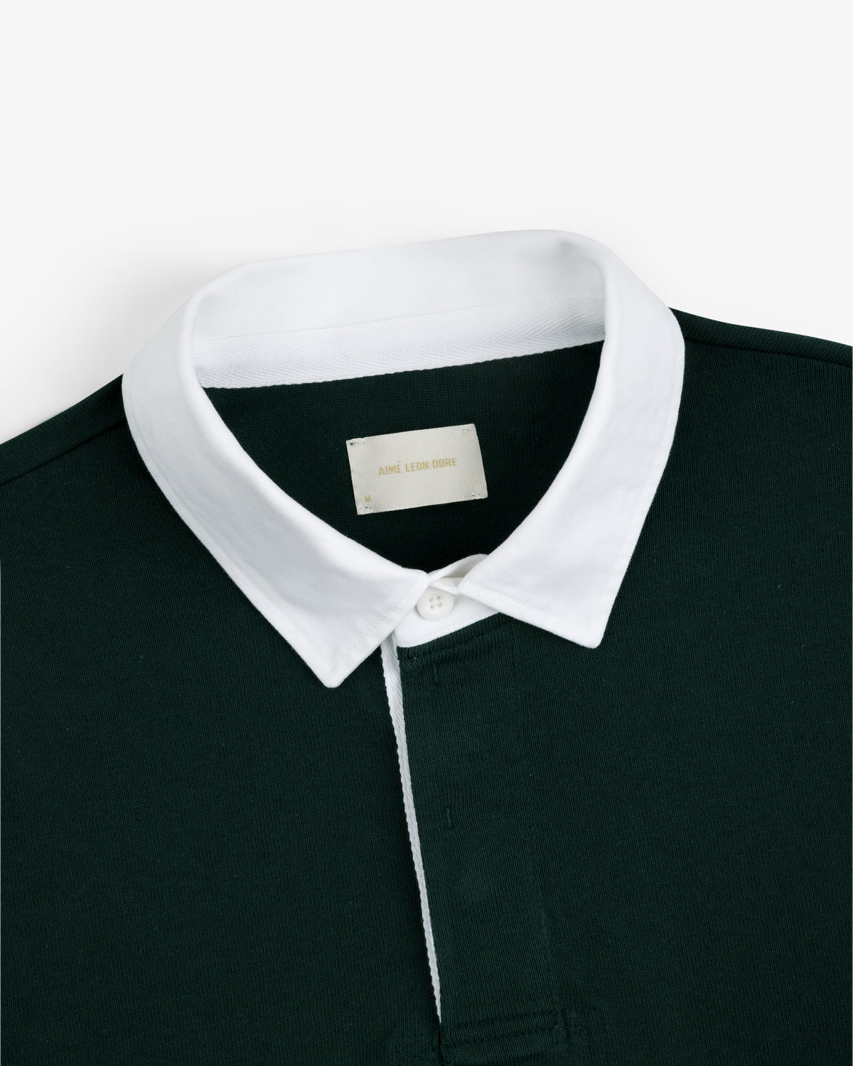 Script Paneled Rugby in dark green with a white collar and visible neckline label, shown on a plain background.