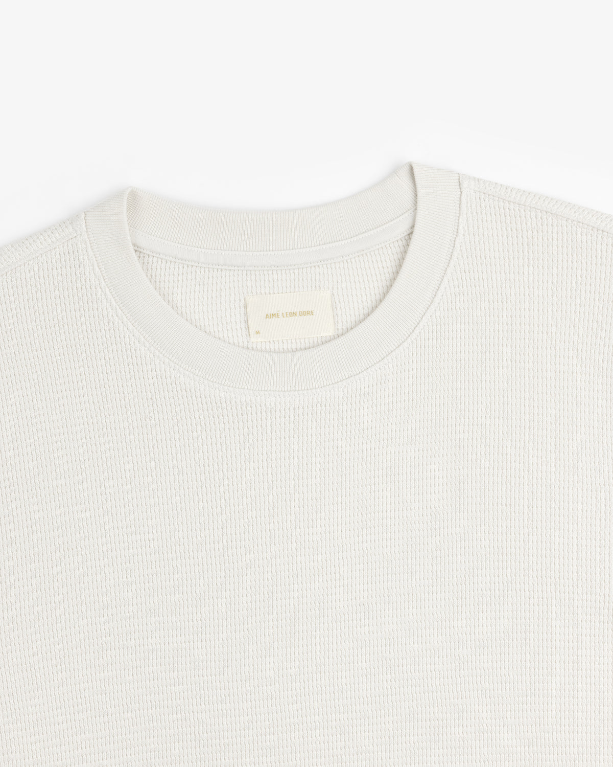 Close-up of a textured, light-colored Long-Sleeve Waffle Thermal crew neck with visible neck label on white background.