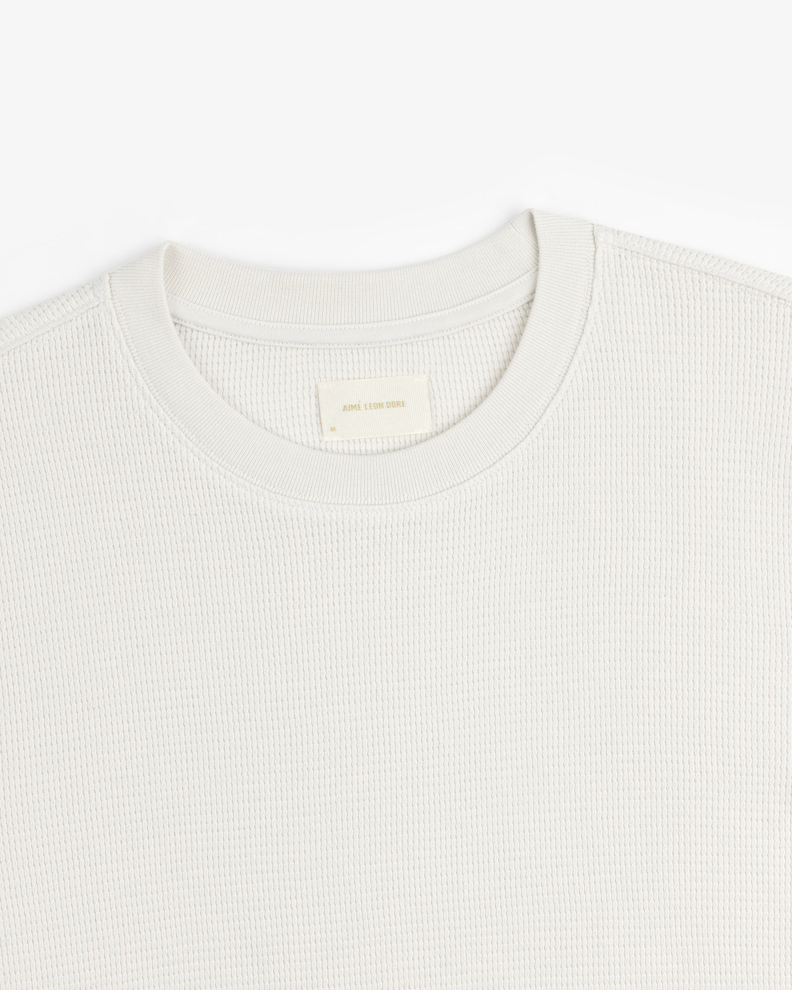 Close-up of a textured, light-colored Long-Sleeve Waffle Thermal crew neck with visible neck label on white background.