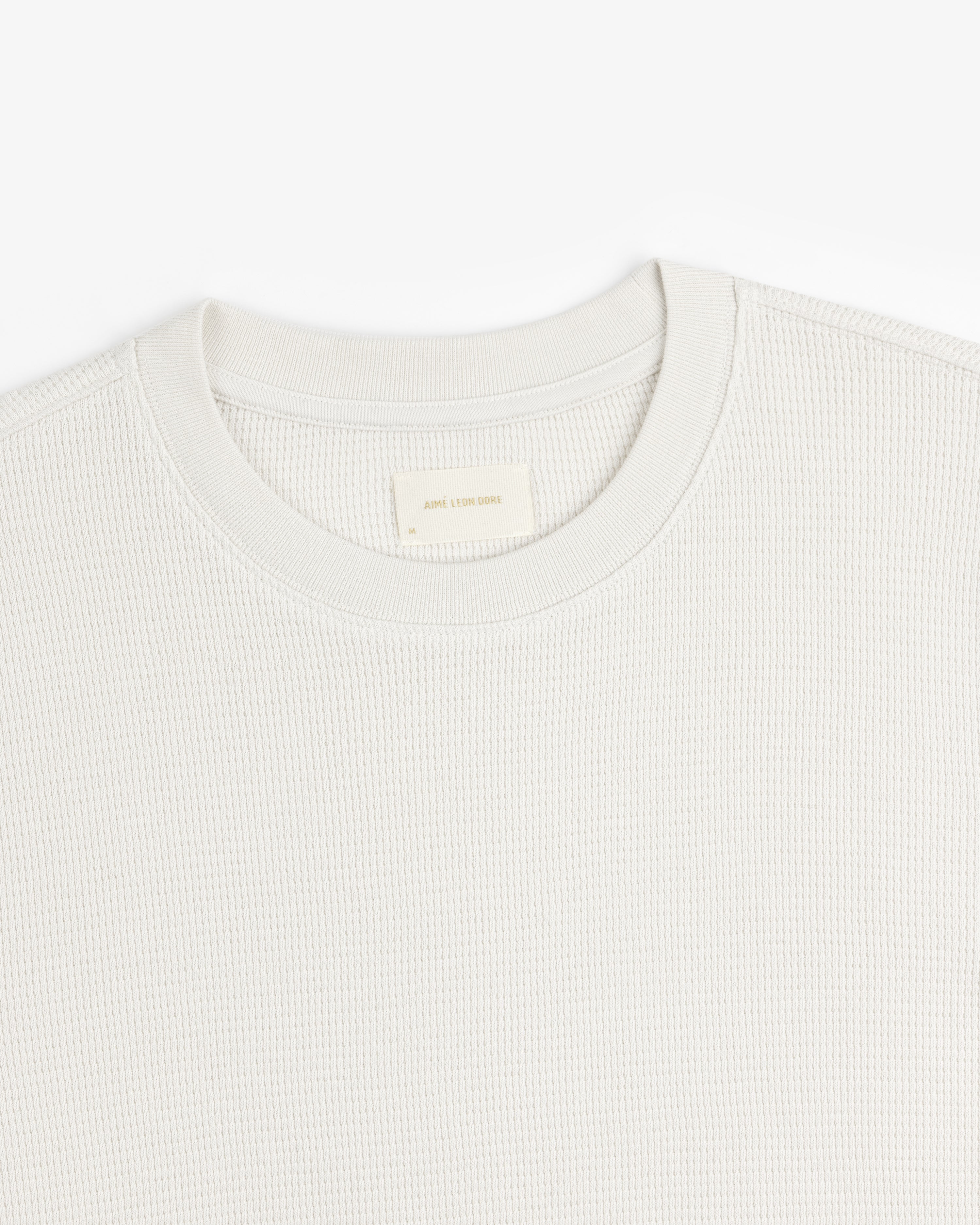 Close-up of a textured, light-colored Long-Sleeve Waffle Thermal crew neck with visible neck label on white background.