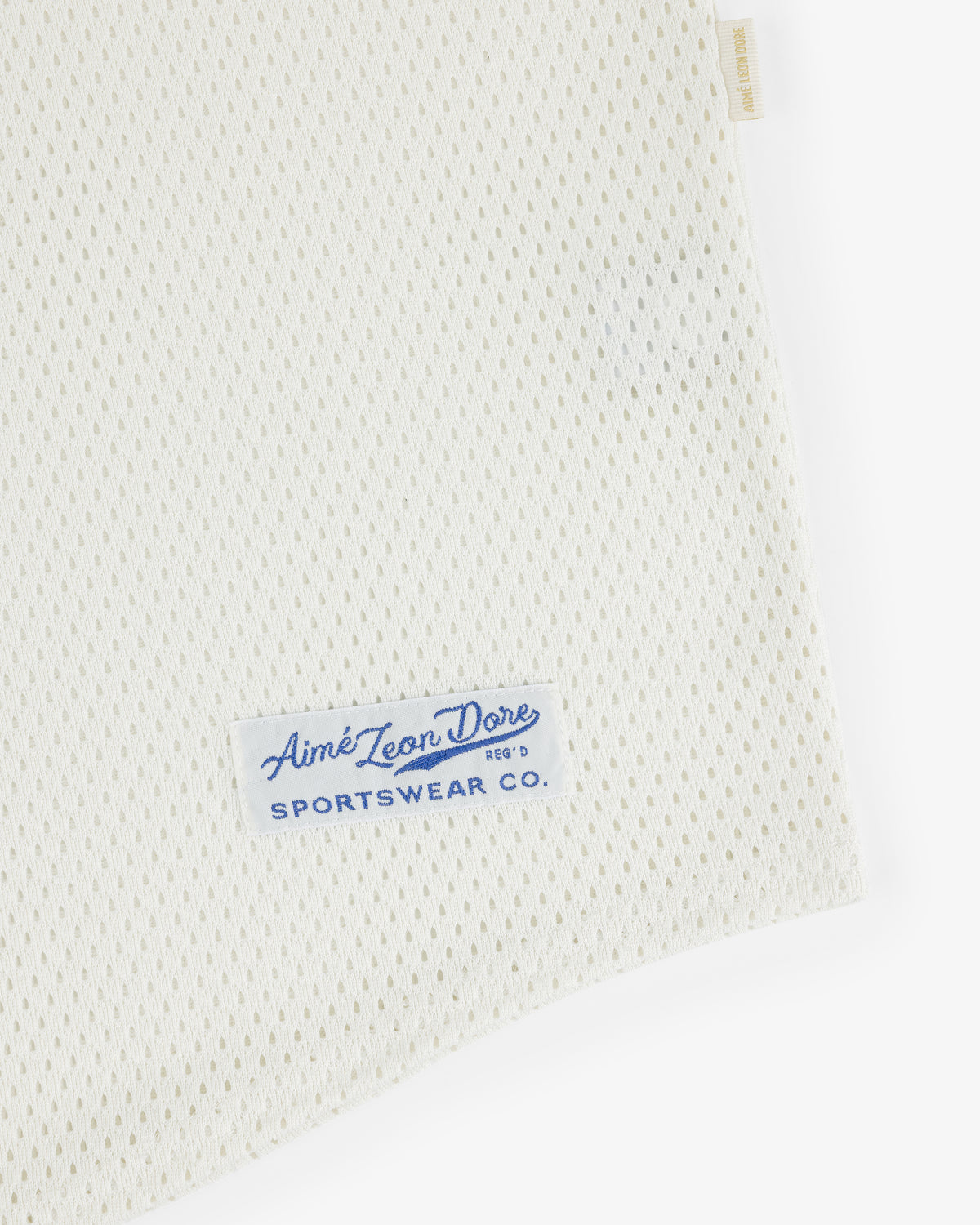 Close-up of white Mesh Batting Practice Jersey with a blue Aimé Leon Dore Sportswear Co. label on the corner.