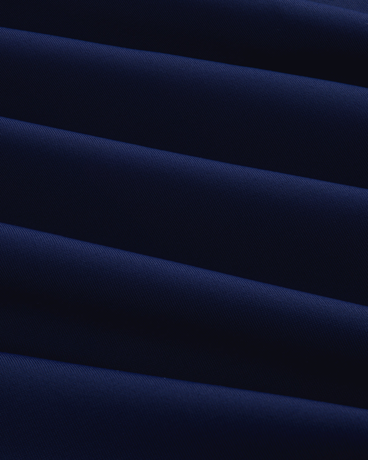 Close-up of Short Sleeve Crest Rash Guard in dark blue with diagonal folds creating light and shadow patterns.