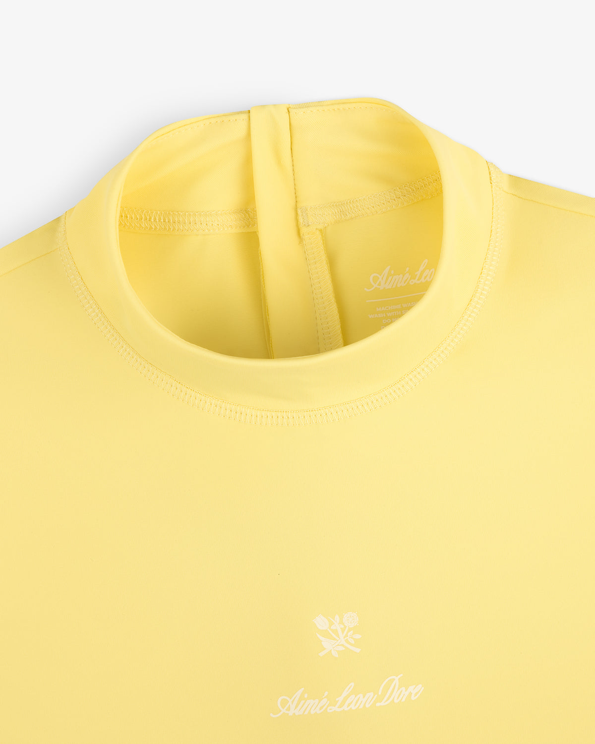 Close-up of a yellow Short Sleeve Crest Rash Guard with a white logo and floral graphic on the chest.