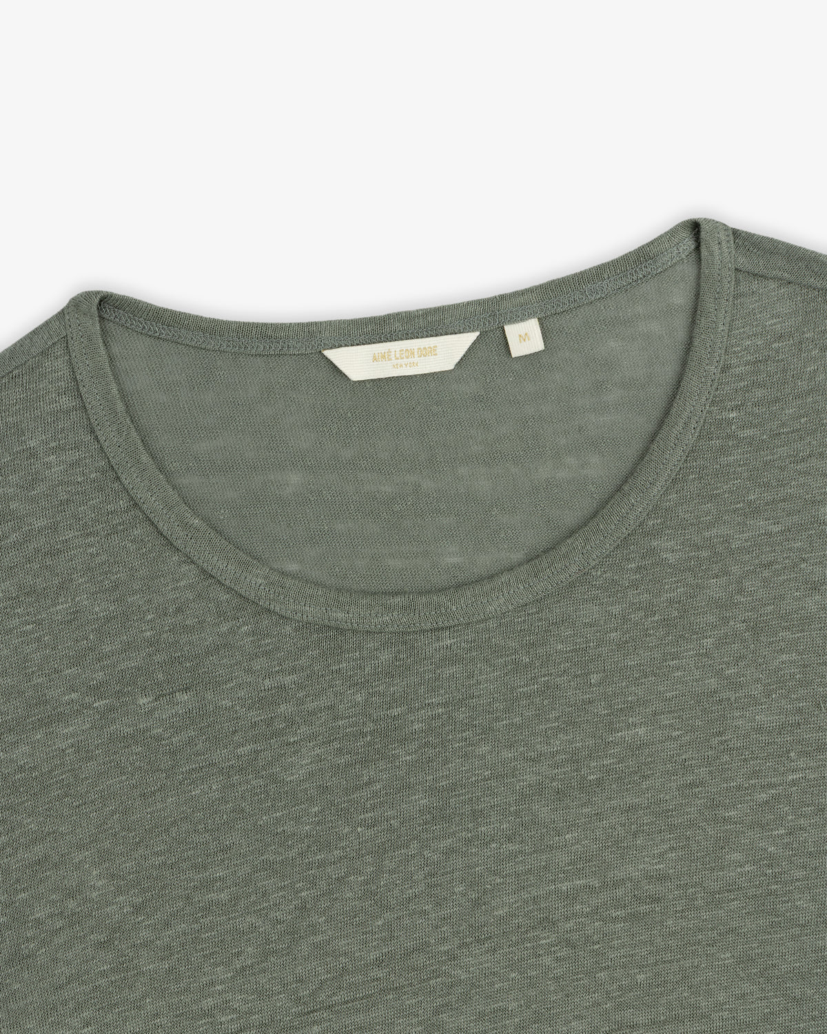 Close-up of a sage green Linen Tee with a small beige size label visible inside the crew neckline.