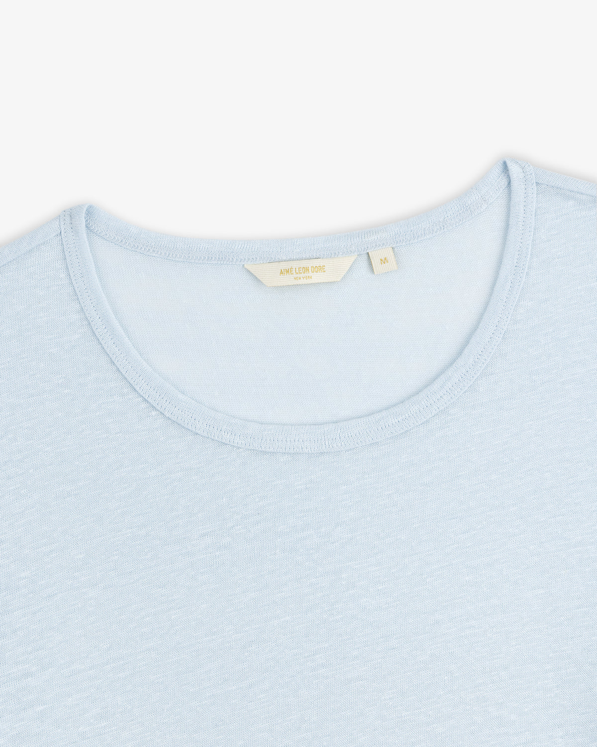 Linen Tee in light blue with a cream-colored label inside the collar, shown on a white background.