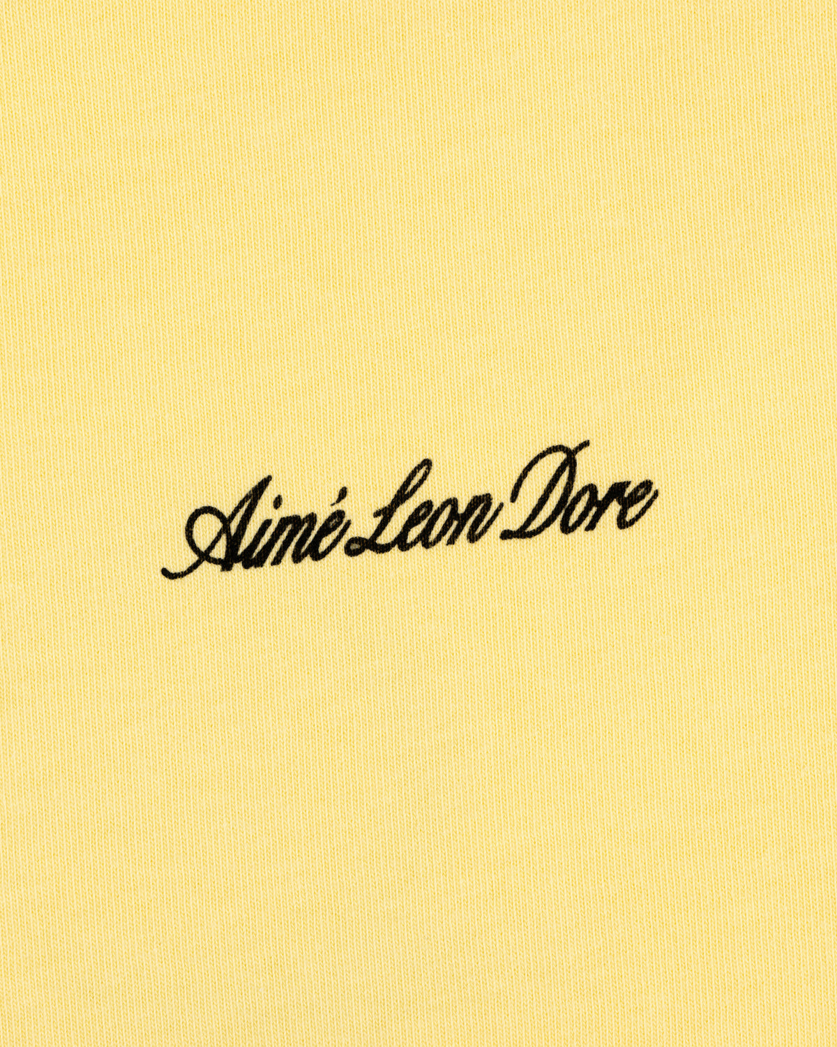 Yellow Super Cub Tee with Aimé Leon Dore in black cursive text at the center.