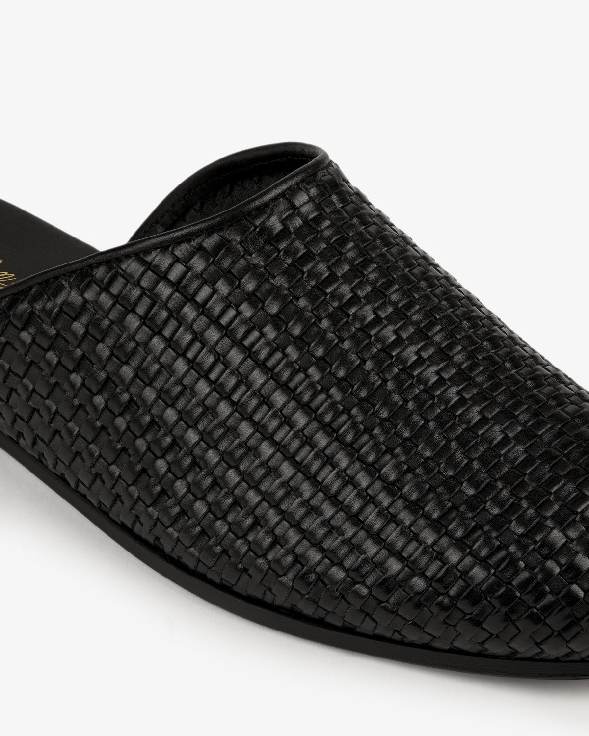 Close-up of the Leather Raffia Mule, a black woven leather slip-on, against a white background.