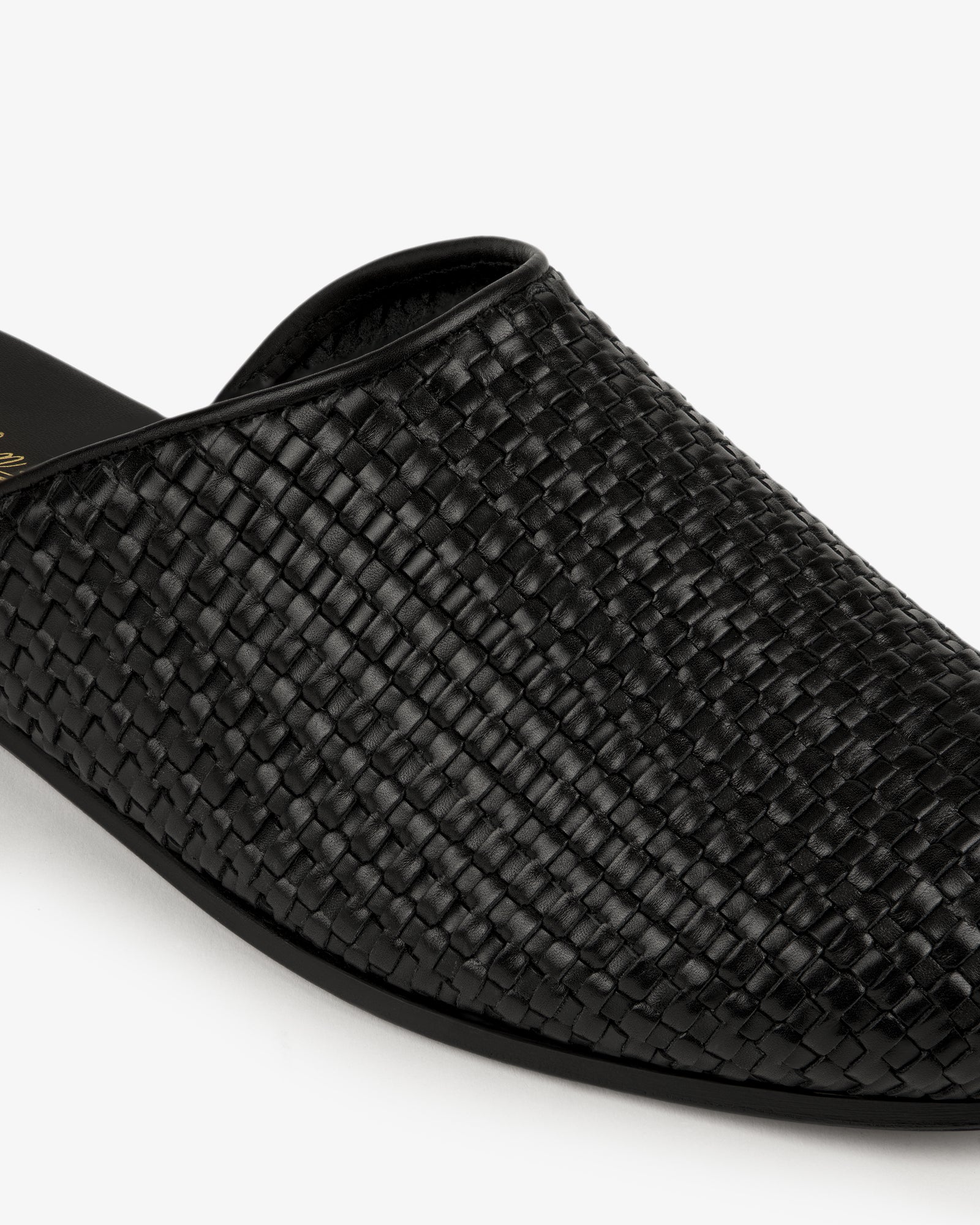 Close-up of the Leather Raffia Mule, a black woven leather slip-on, against a white background.