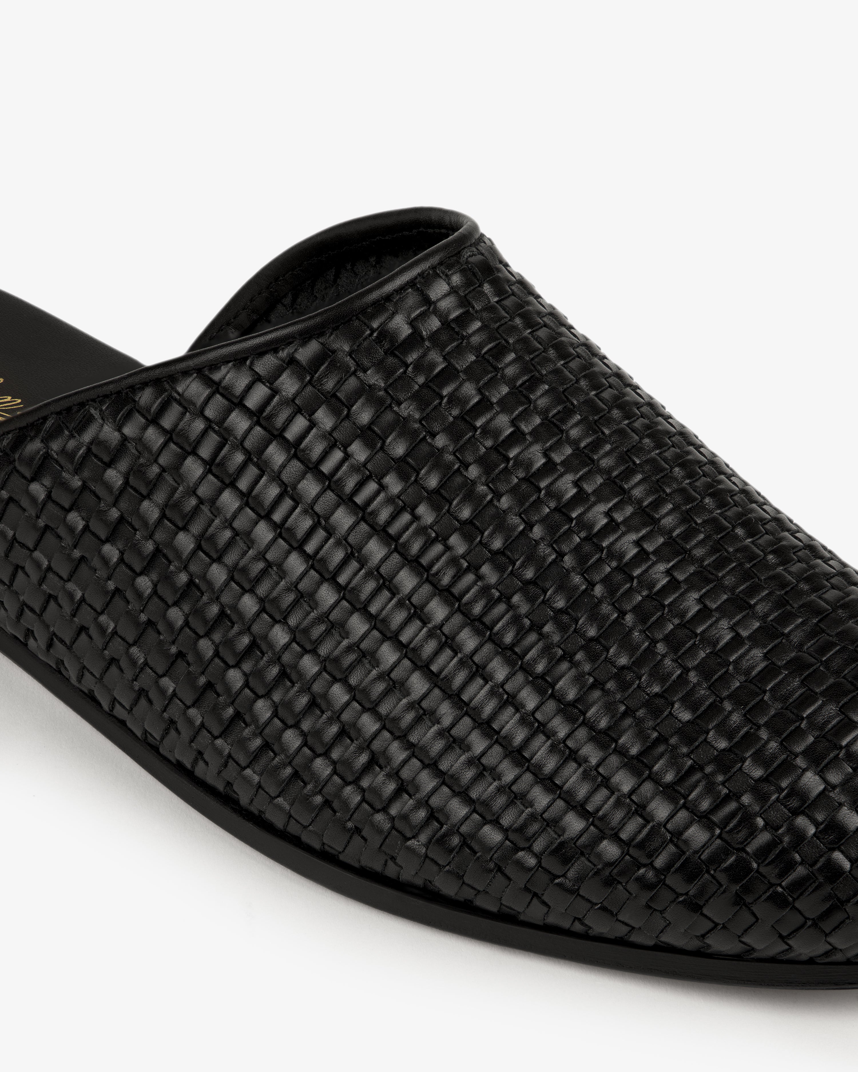 Close-up of the Leather Raffia Mule, a black woven leather slip-on, against a white background.