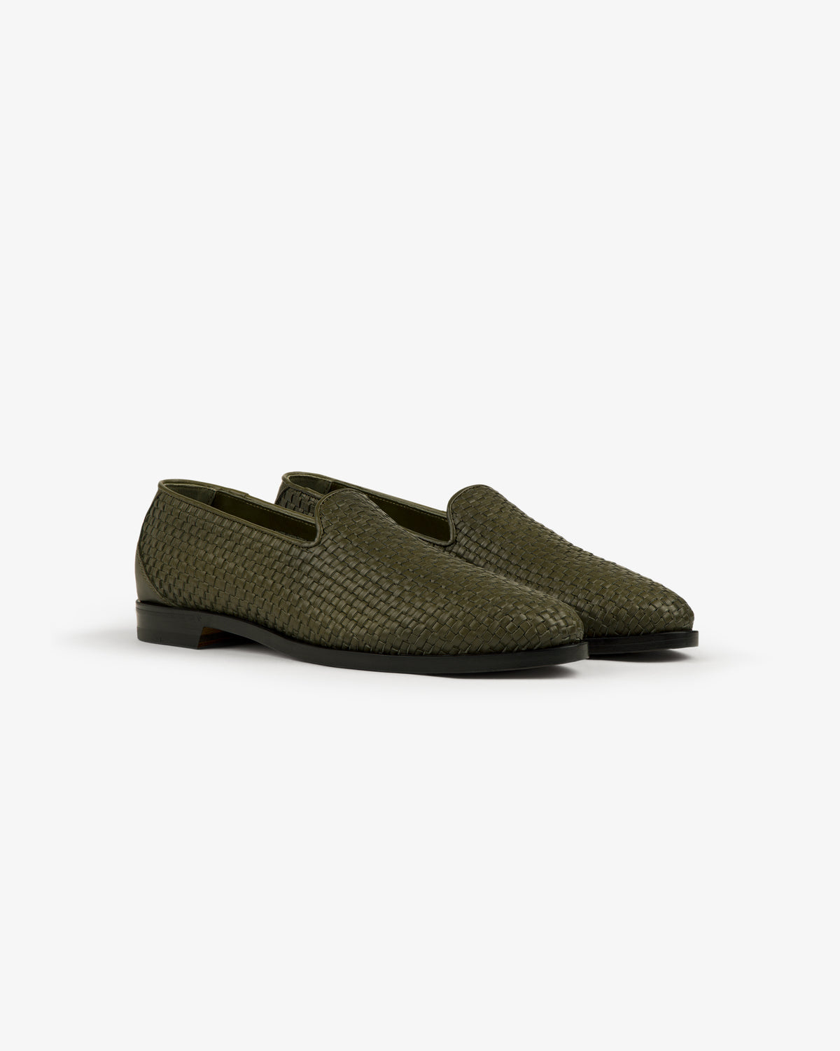 The Leather Raffia Loafer in green features black soles and a woven slip-on design, shown on a white background.