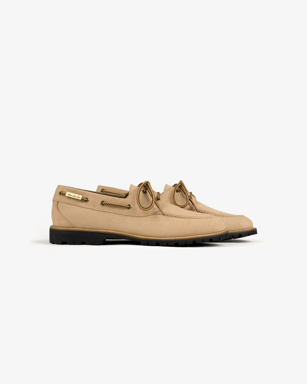 Pápia Boat Shoe: beige leather, brown laces, metal eyelets, black rubber sole on a white background.