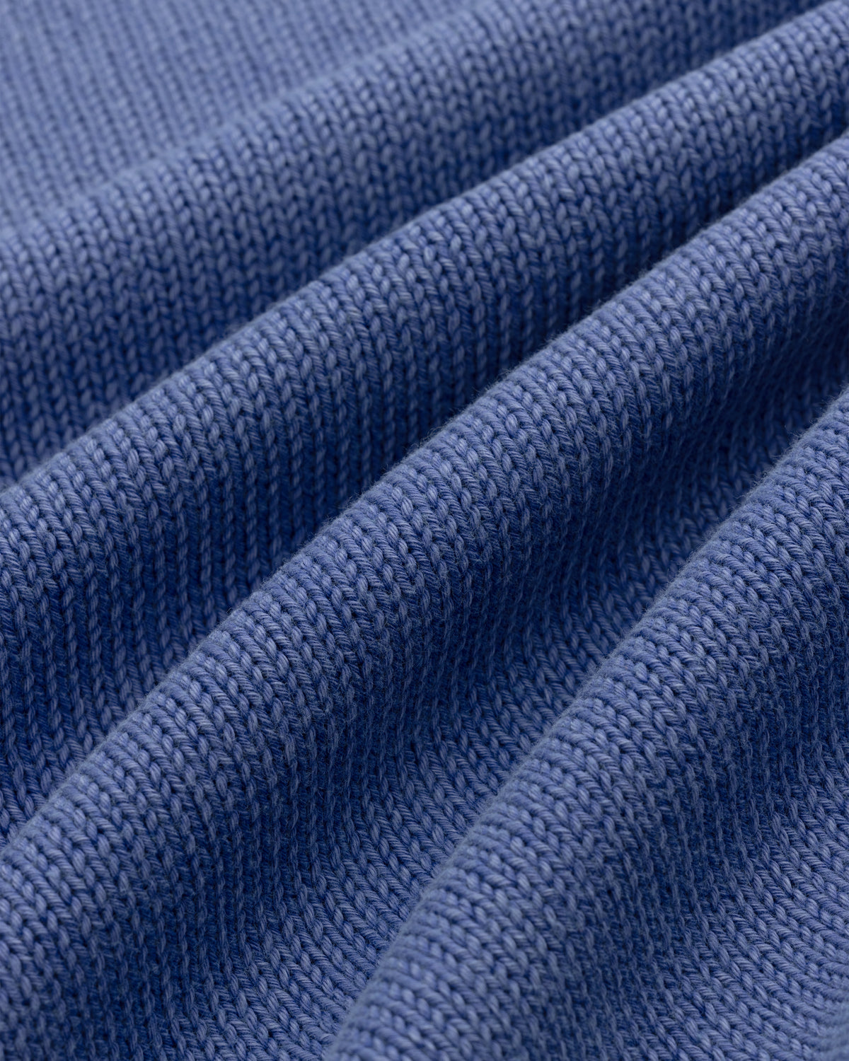 Close-up of Washed Inside Out Sweater’s blue knit fabric, showing visible texture and horizontal folds.