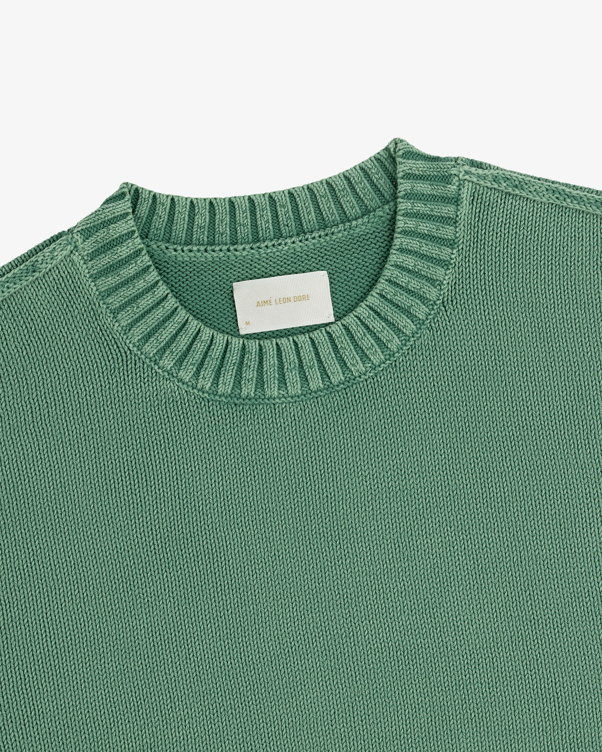 Close-up of the Washed Inside Out Sweater in green, featuring a ribbed neckline and white collar label.