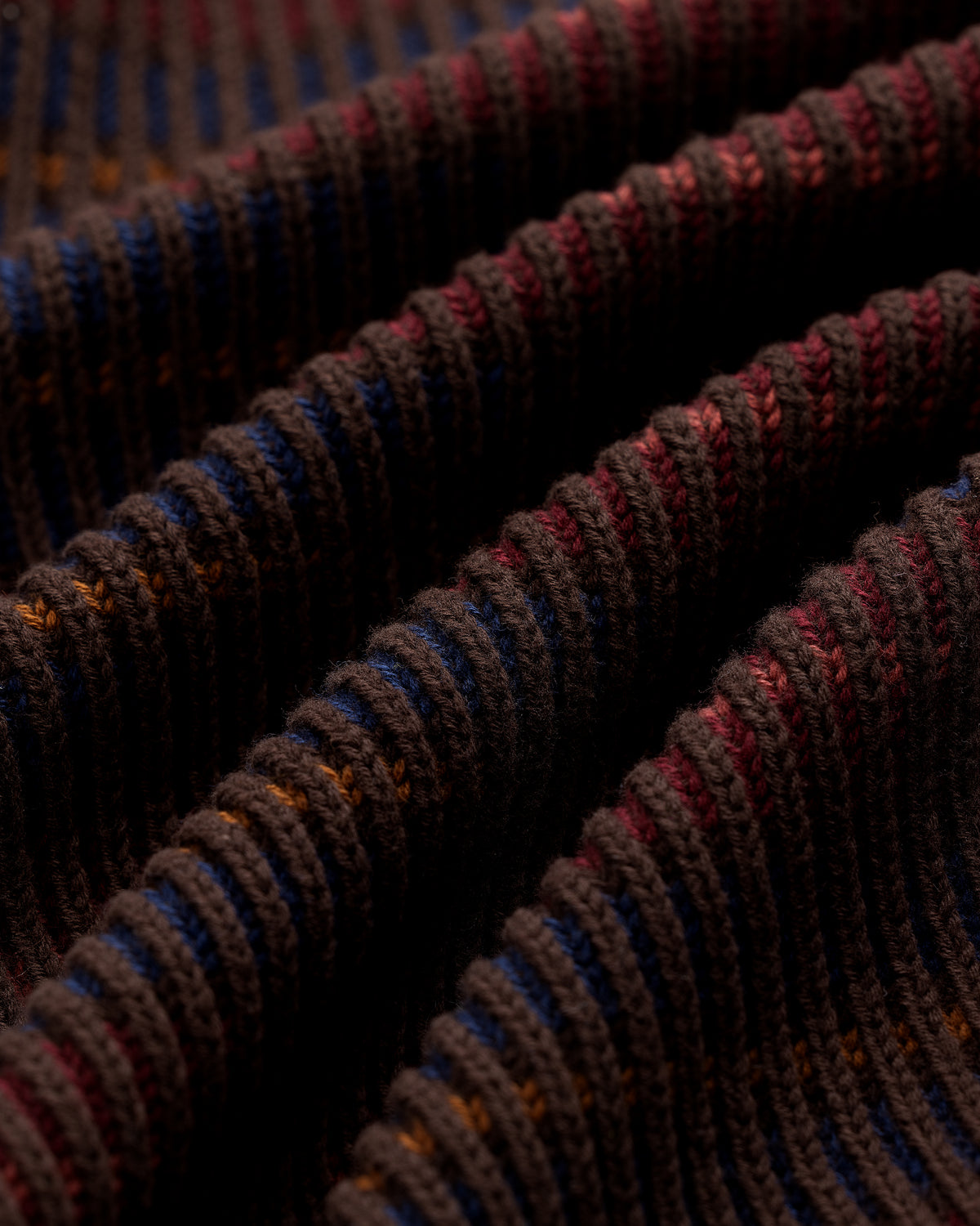 Close-up of Multi Color Knit Track Sweater with brown ribbed fabric and blue, orange, and red striped wavy folds.