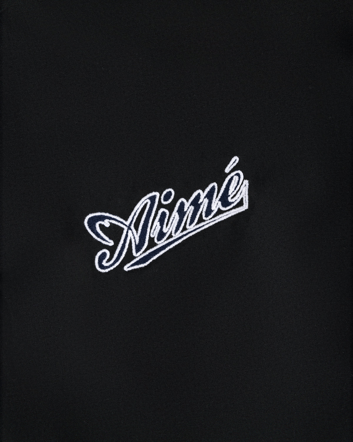 White Aimé script embroidered on black fabric of the Reversible Knit Bomber Jacket.