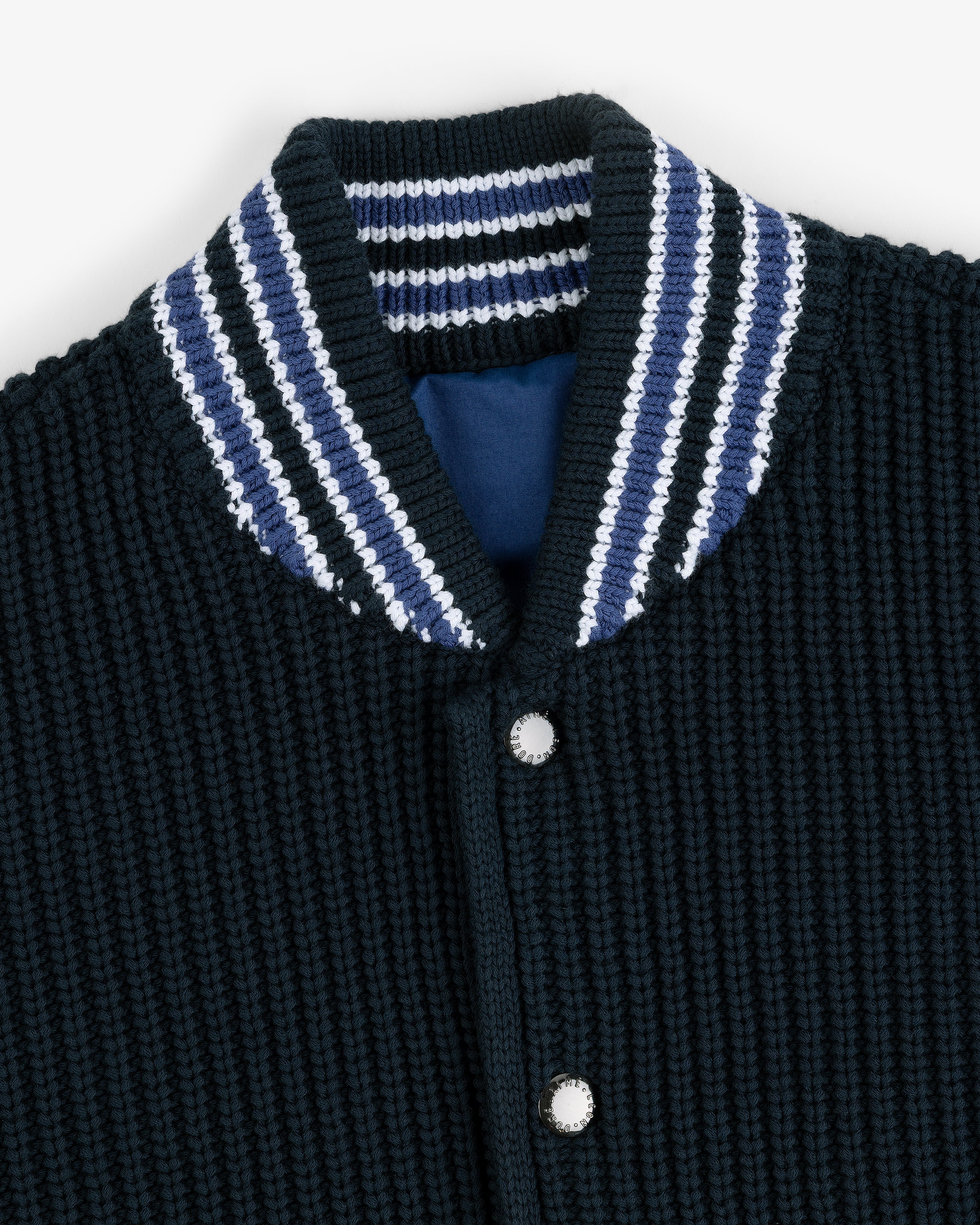 Close-up of a Reversible Knit Bomber Jacket with a textured black finish, striped collar, and silver snap buttons.