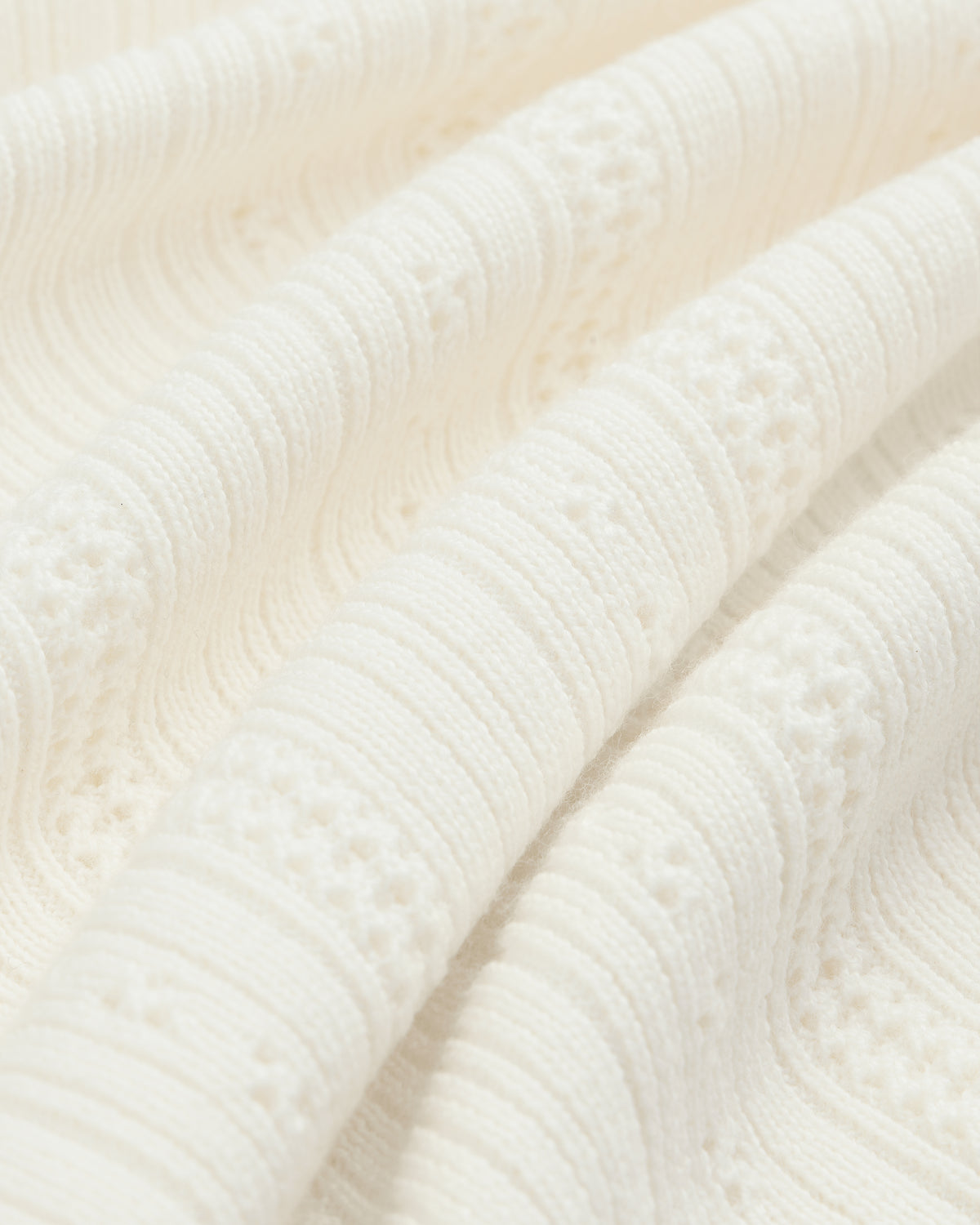 Close-up of textured Merino Wool Eyelet Tee featuring off-white raised, wavy knit patterns and intricate details.