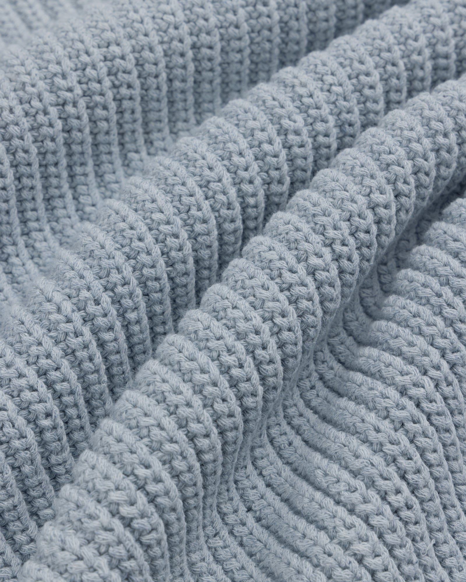Close-up of the Knit Denim Crewneck Sweater's light blue, ribbed knit fabric with gentle textured folds.