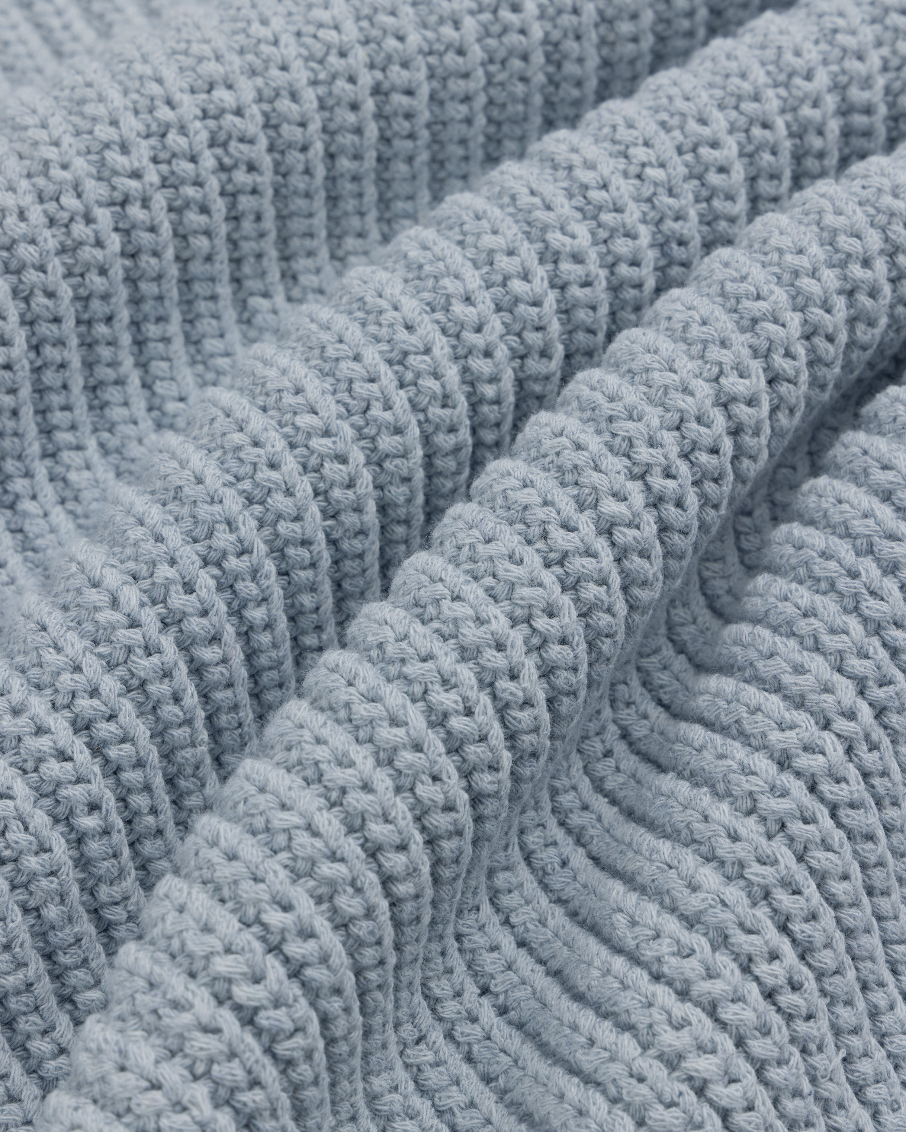 Close-up of the Knit Denim Crewneck Sweater's light blue, ribbed knit fabric with gentle textured folds.