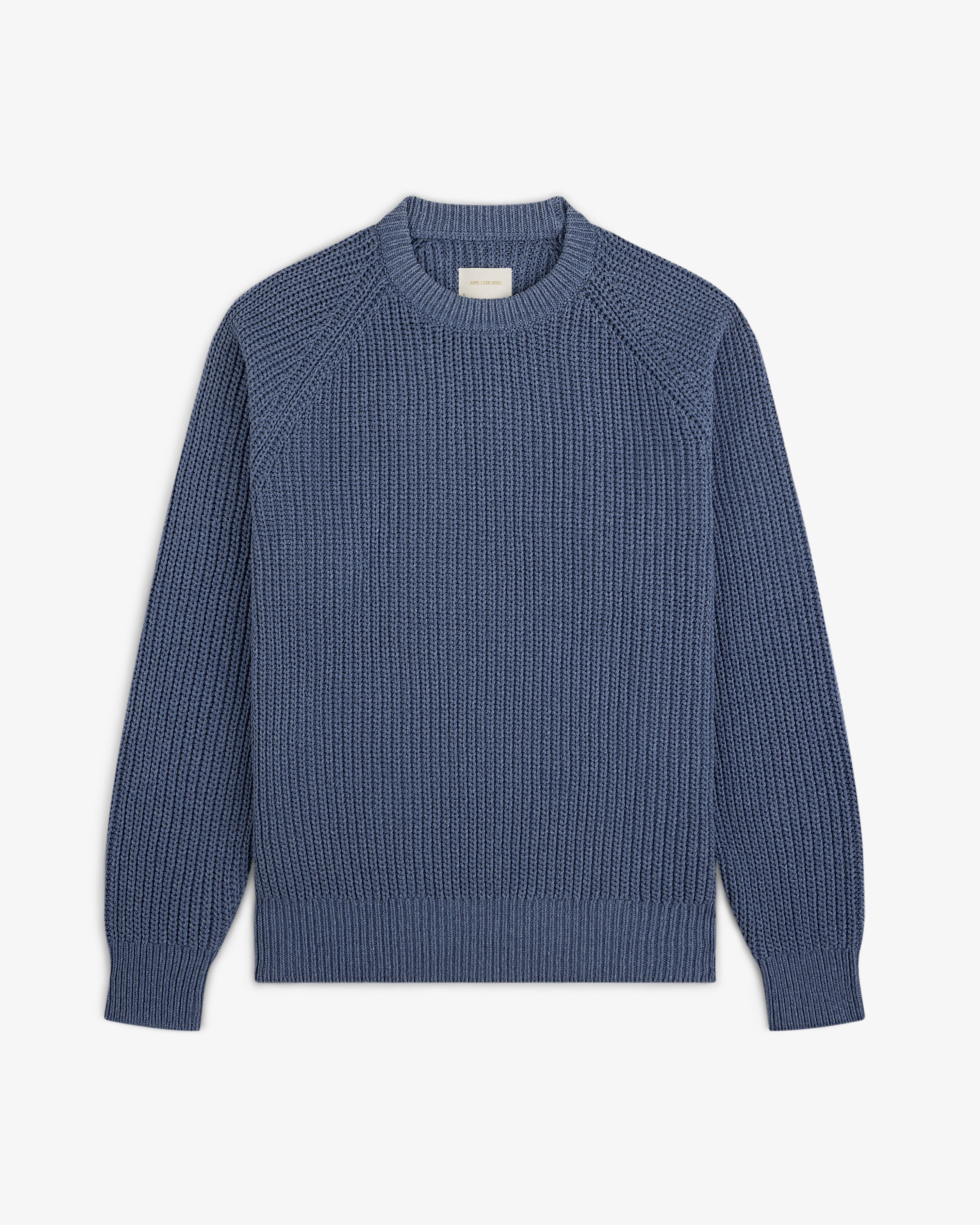 The Knit Denim Crewneck Sweater features long sleeves, ribbed cuffs, and a textured pattern, shown on a white background.