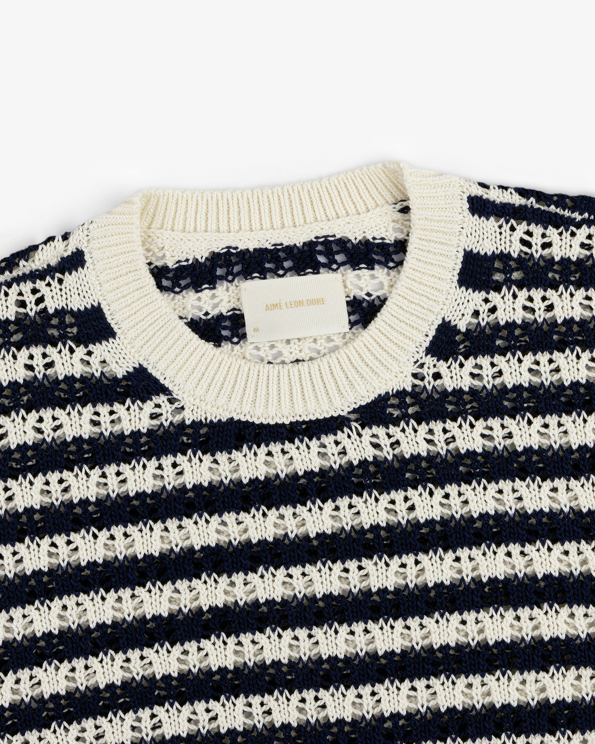 The Skáfos Sweater is navy blue with white stripes, a ribbed collar, and a visible label inside the neckline.