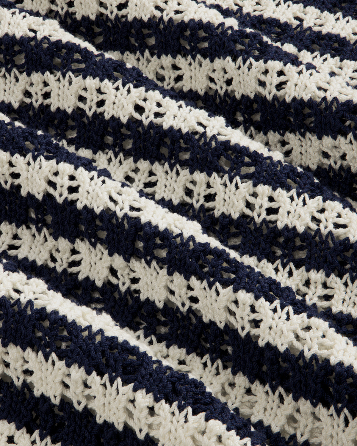 Close-up of the Skáfos Sweater’s textured fabric with diagonal navy and white crocheted stripes.