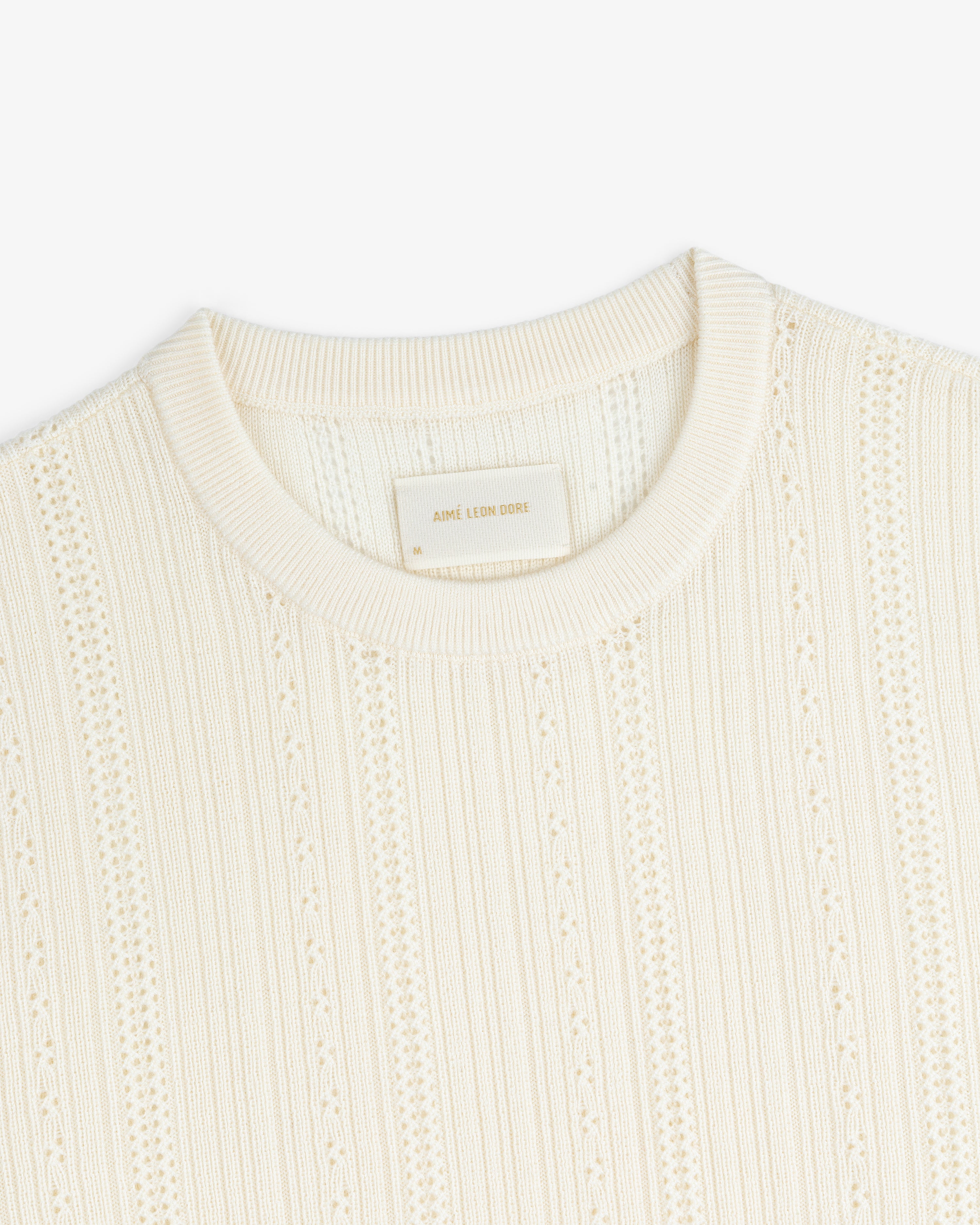 Close-up of the Merino Wool Eyelet Tee in cream, featuring textured knit, ribbed crew neck, and vertical patterns.