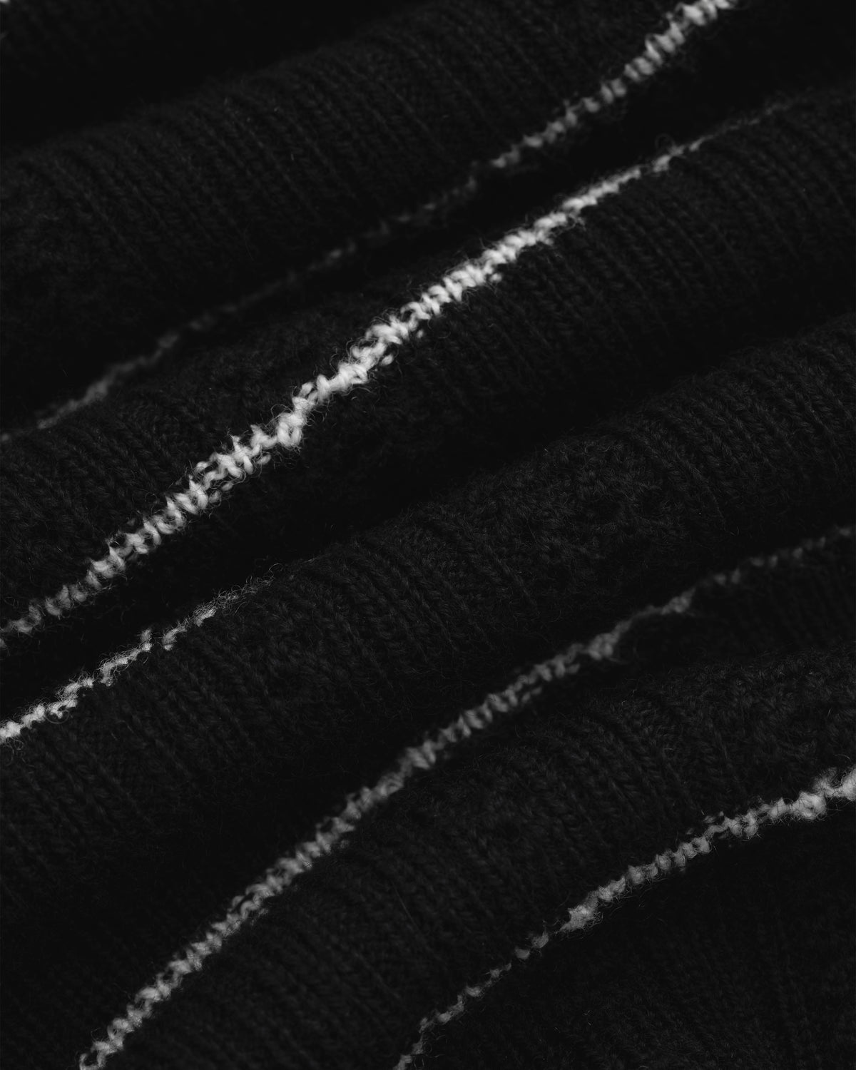 Close-up of the Merino Wool Eyelet Tee in black, featuring ribbed fabric with white stitched stripes across the folds.