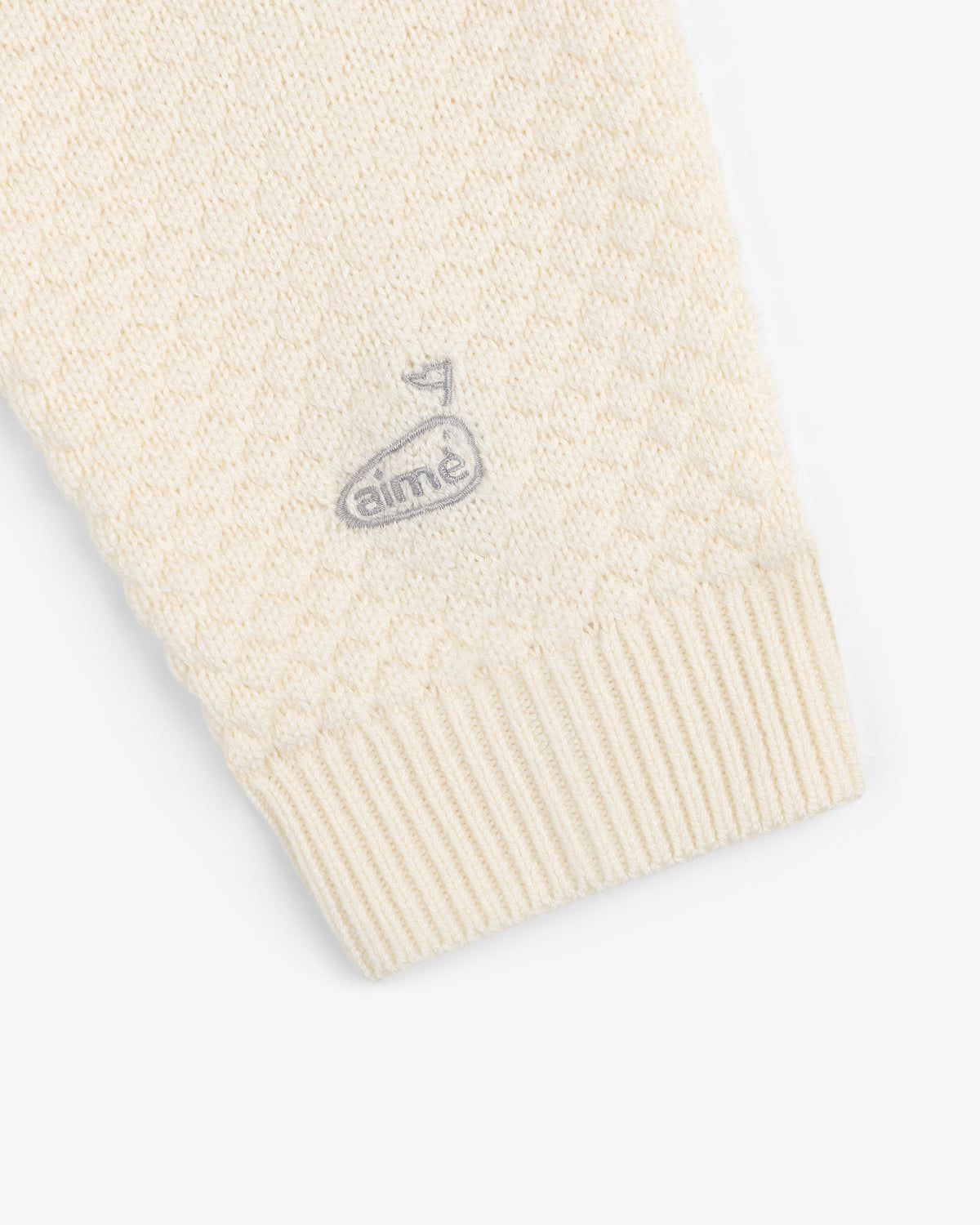 Close-up of the ALD Golf Clubhouse Sweater sleeve featuring a small embroidered logo near the cuff.