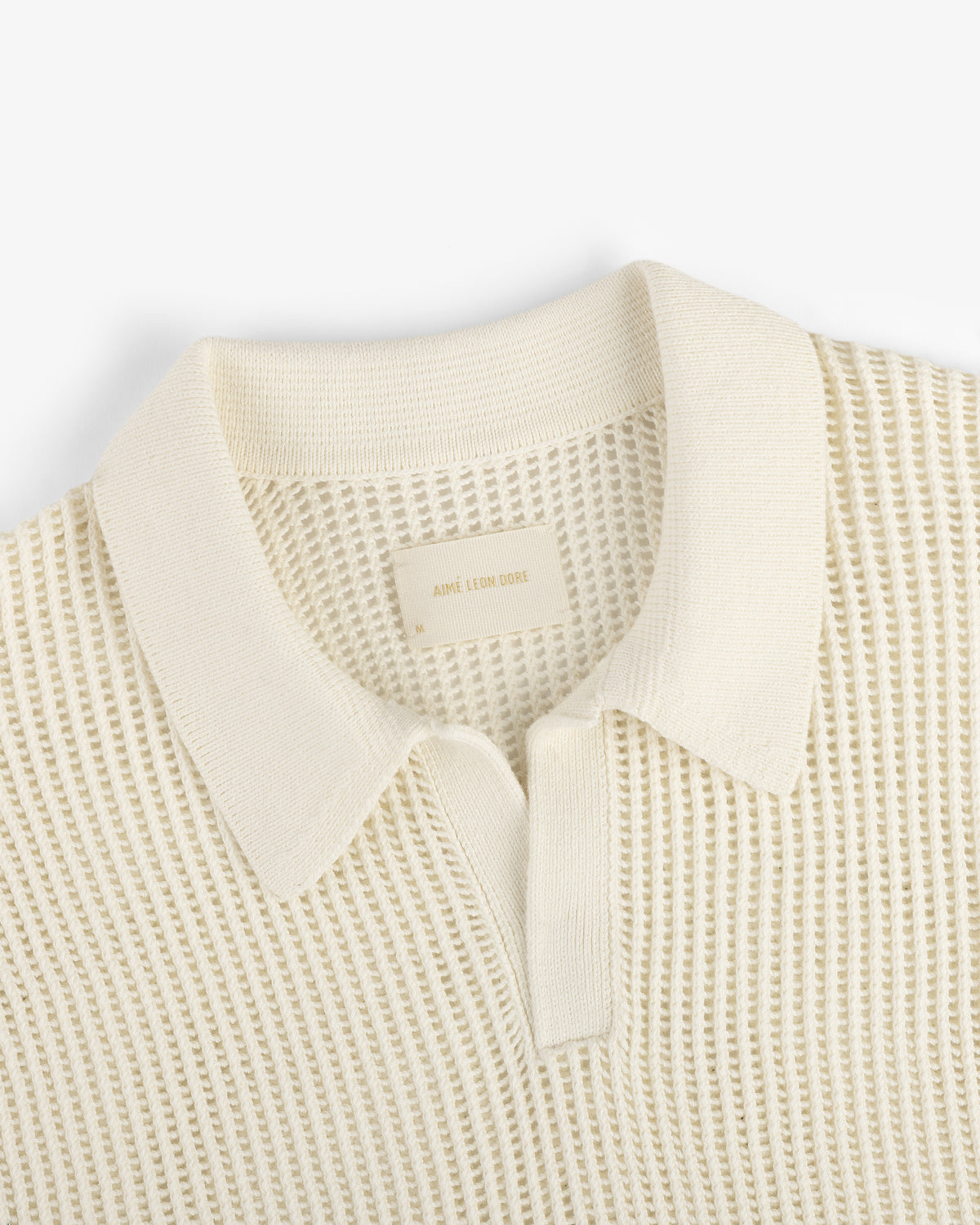 Mesh Knit Polo in cream with textured knit, collar, and short buttoned placket, laid flat on a white background.