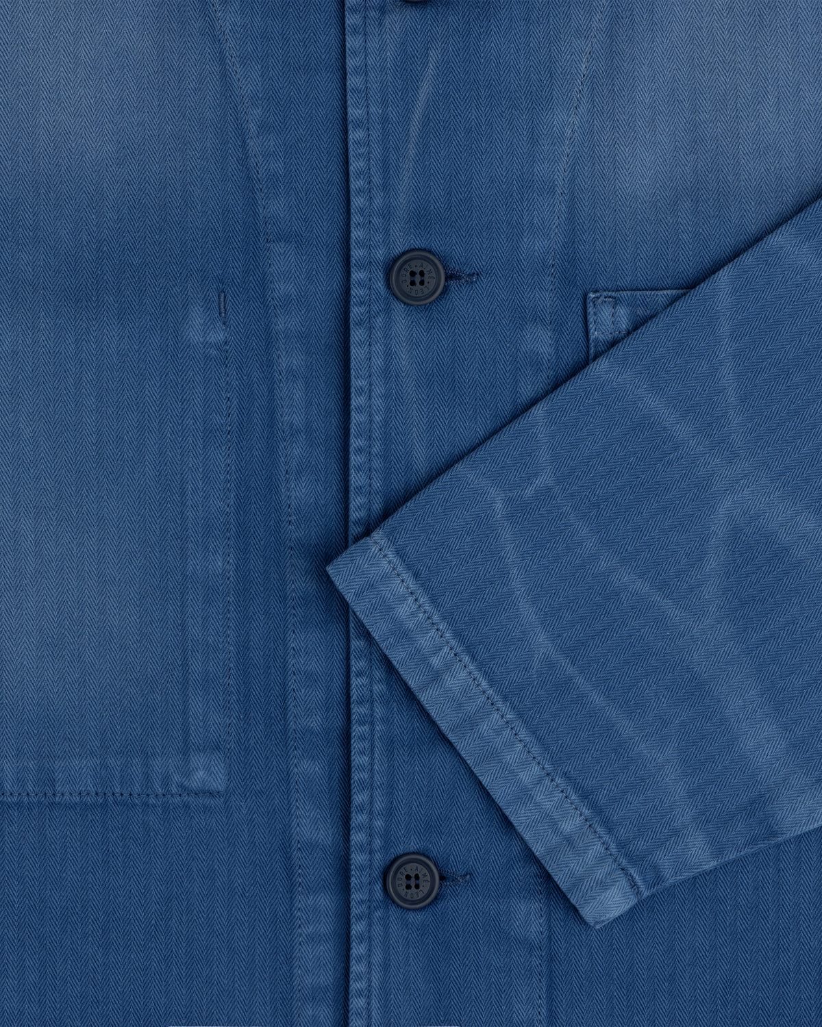 Close-up of the Sun Faded Chore Jacket in blue denim with black buttons, chest pocket, and folded sleeve detail.