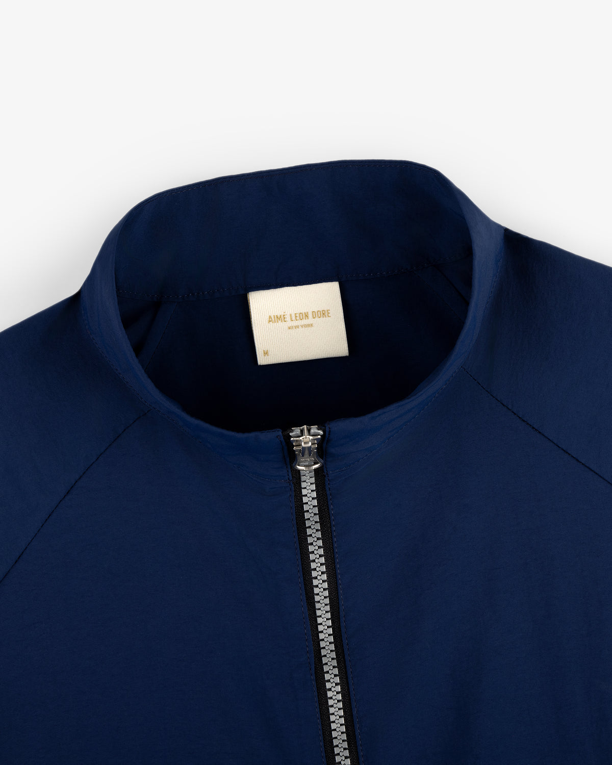 Close-up of the Nylon Packable Windbreaker in navy blue, featuring a silver zipper and AIMÉ LEON DORE collar label.