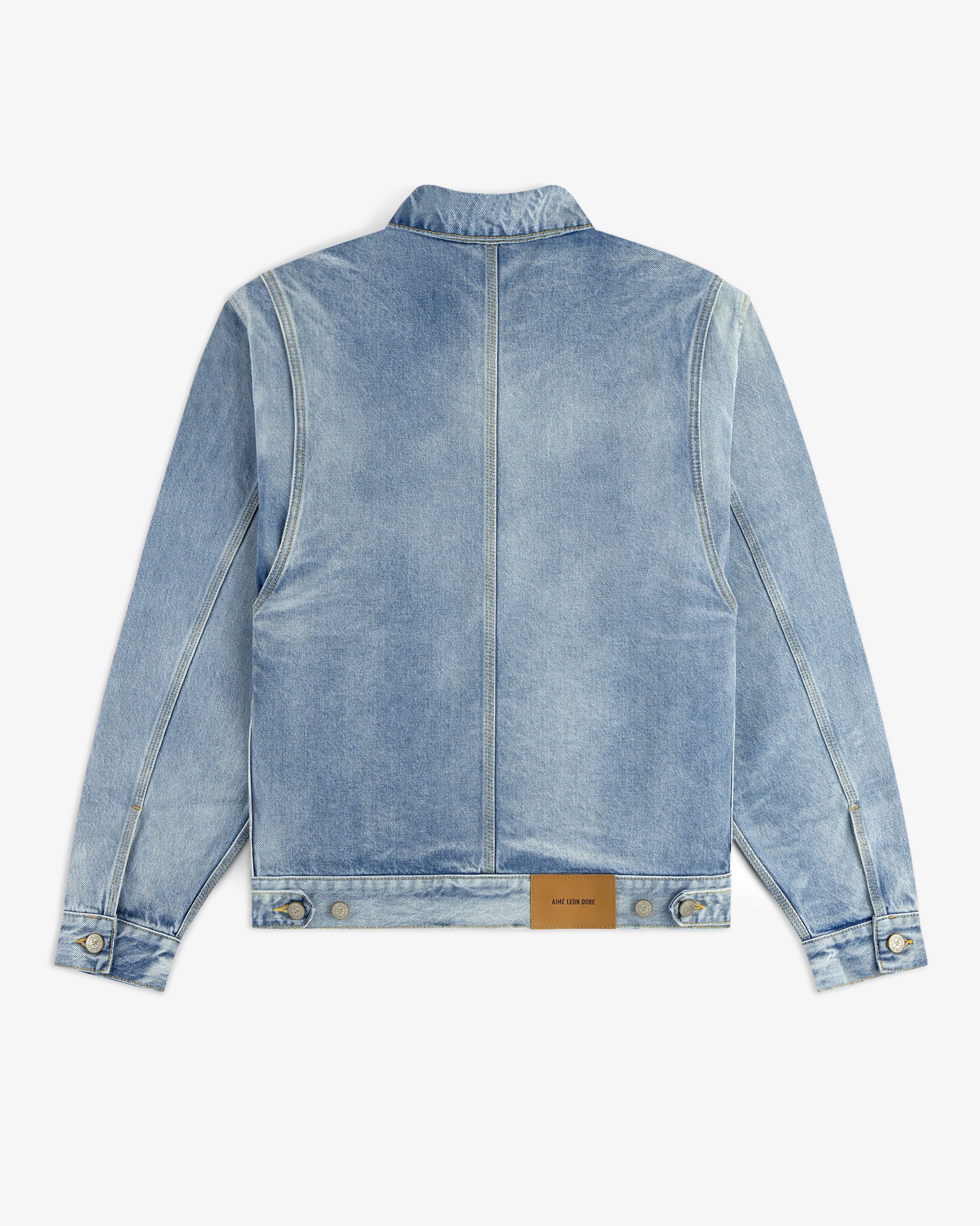 The Denim Trucker Jacket is light blue with a tan leather patch near the bottom hem on the back.