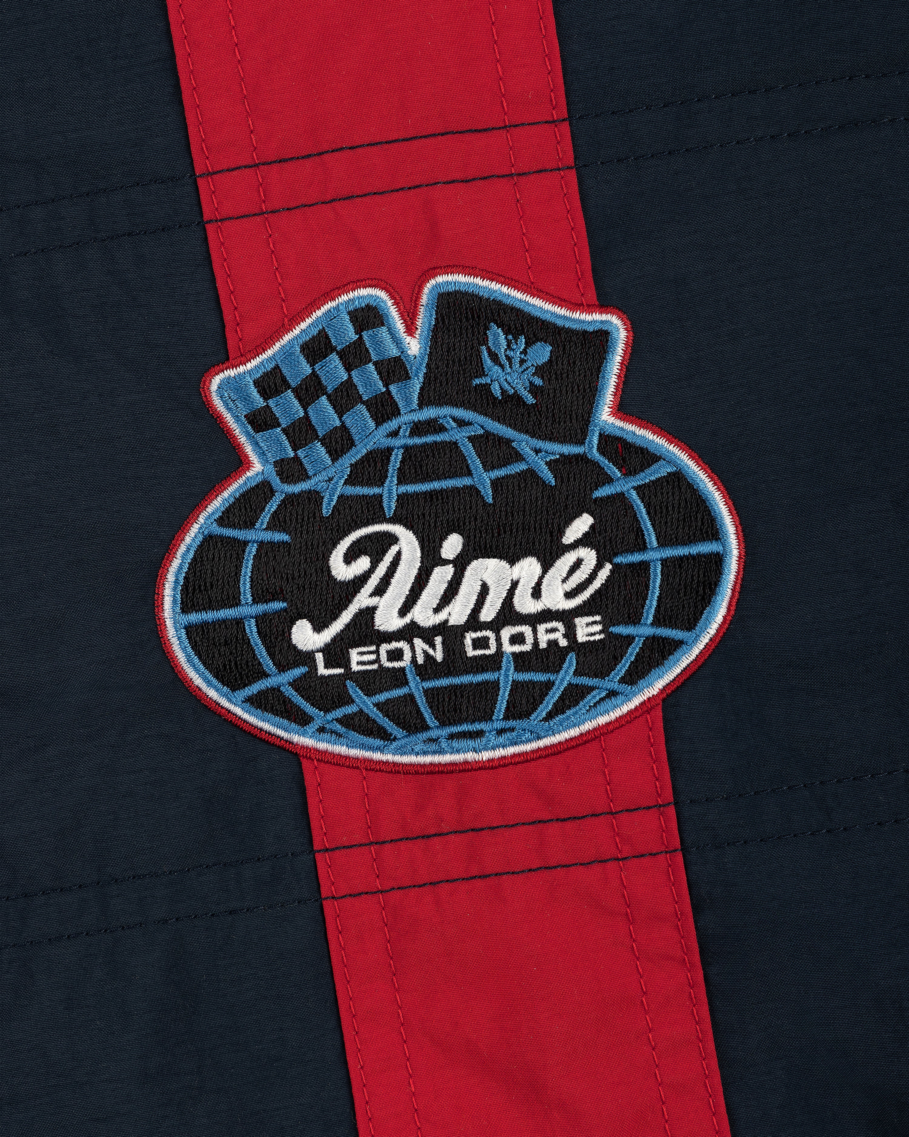 A patch on the Nylon Moto Jacket features Aimé Leon Dore on a globe, a checkered flag, and laurel on navy with red stripe.