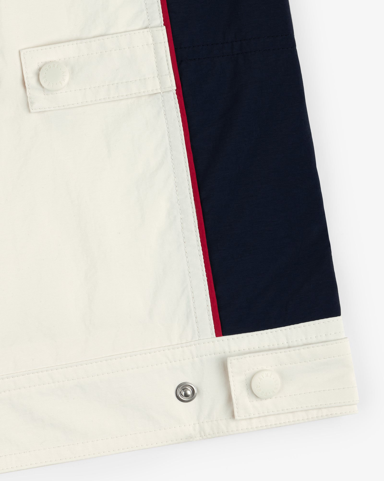 Close-up of Nylon Moto Jacket's hem with white, navy, and red color blocks, buttons, and snap fasteners.