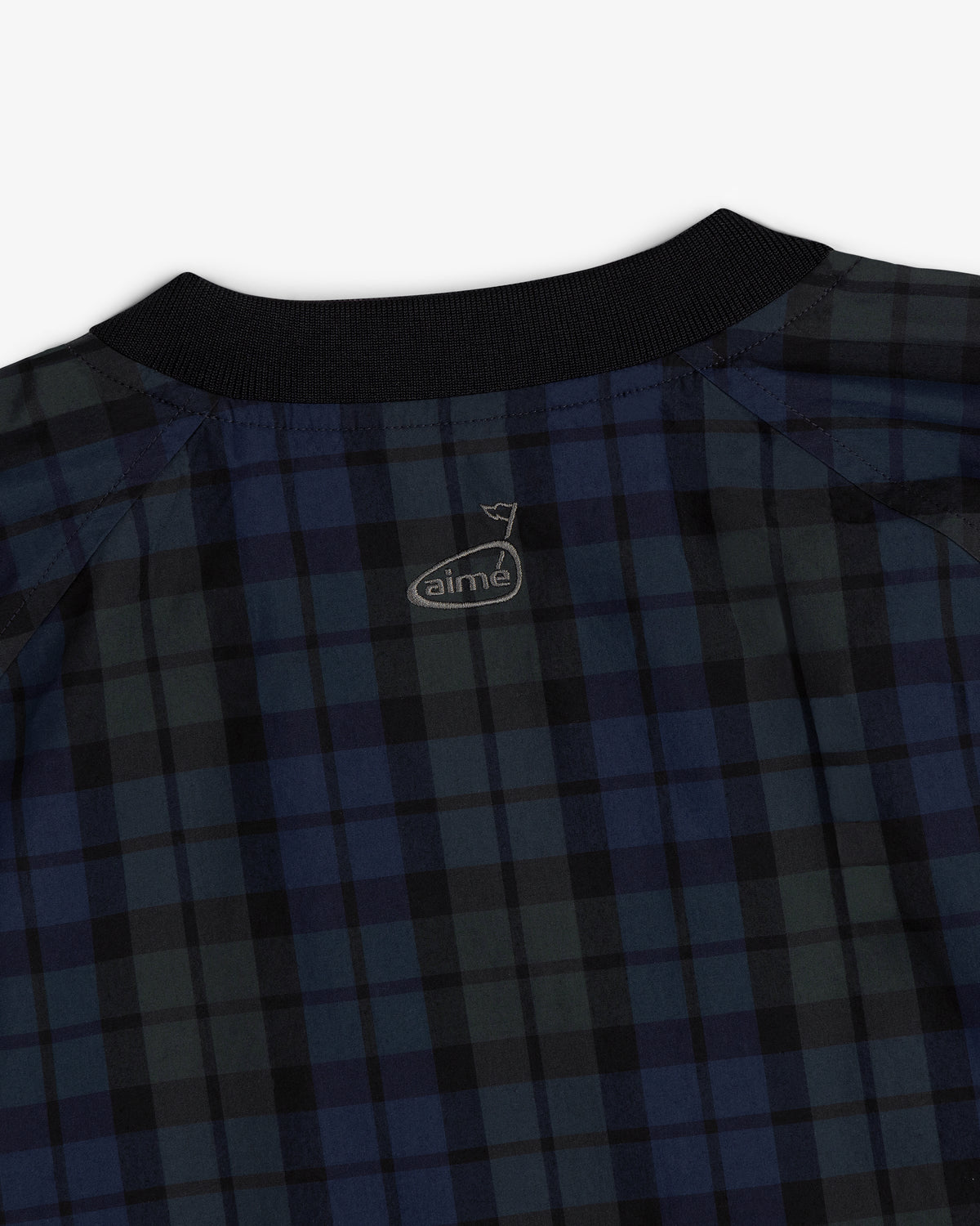 Close-up of the ALD Golf Blackwatch Pullover, a dark blue and black plaid shirt with a black collar and small logo.