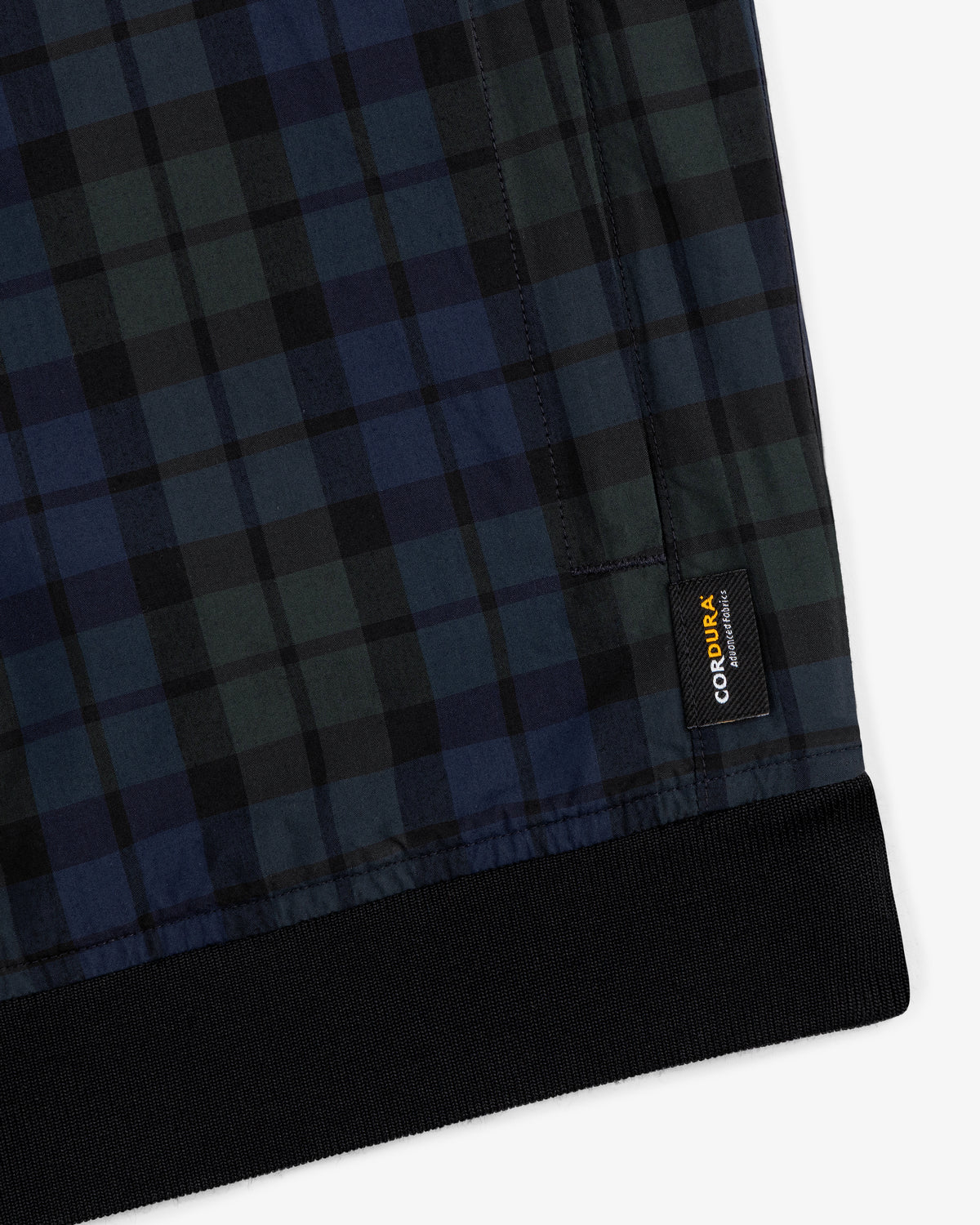 Close-up of the ALD Golf Blackwatch Pullover with a black CORDURA label and black ribbed hem.