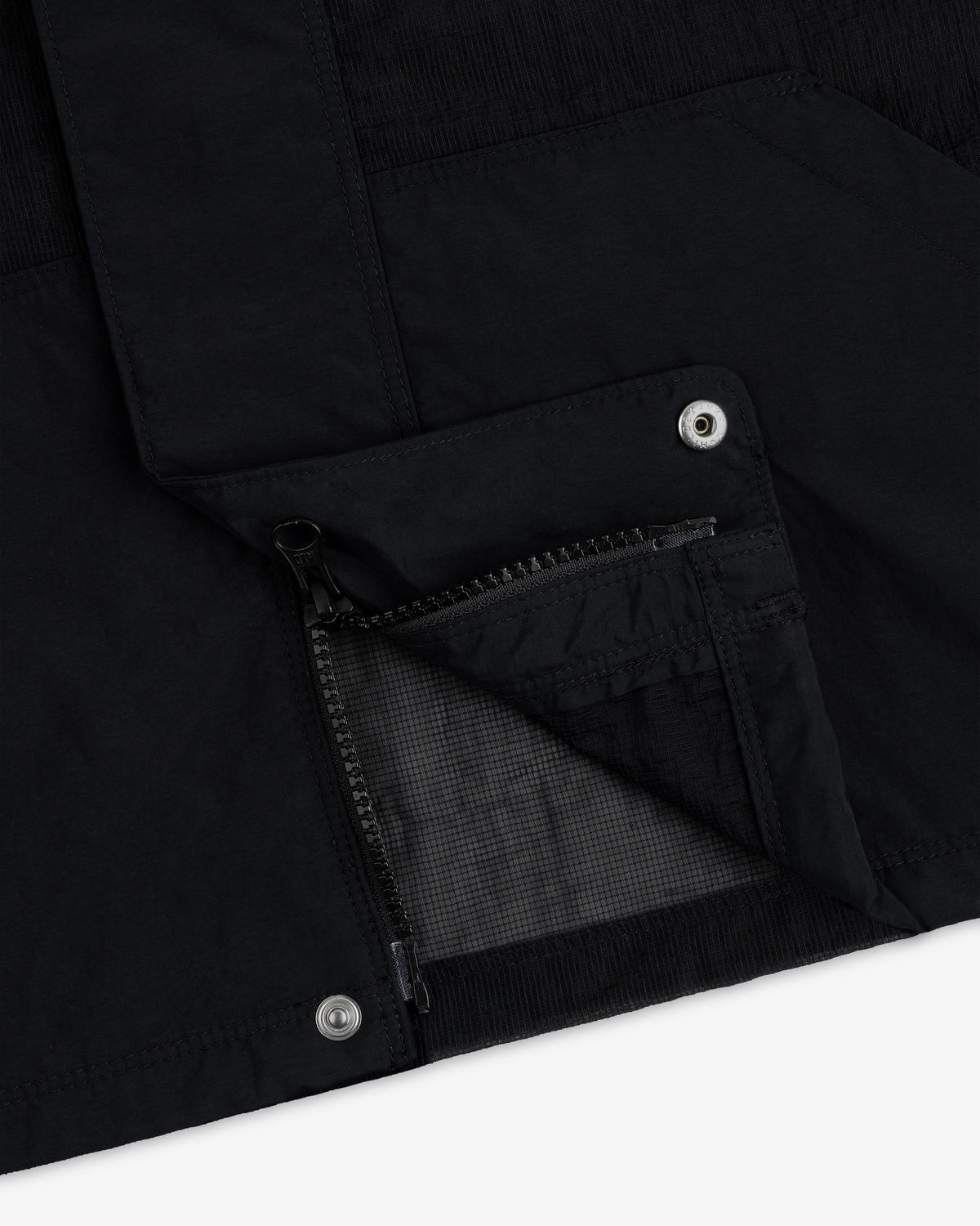 Close-up of the Nylon Track Jacket featuring a zippered pocket and metal snap buttons on black fabric.