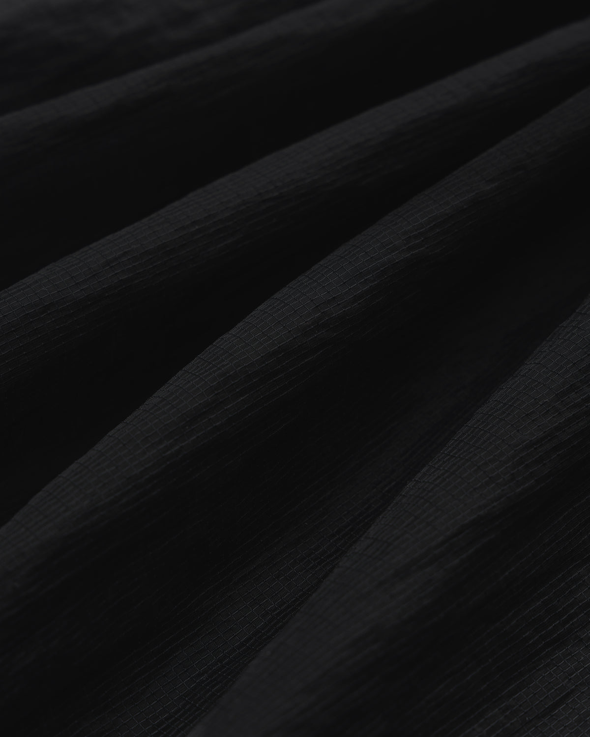 Close-up of black Nylon Track Jacket fabric with a textured, slightly ridged surface and soft, diagonal folds.