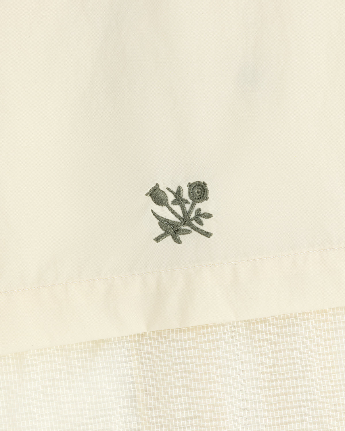 Green floral embroidery on cream nylon track jacket featuring a subtle checked pattern below.
