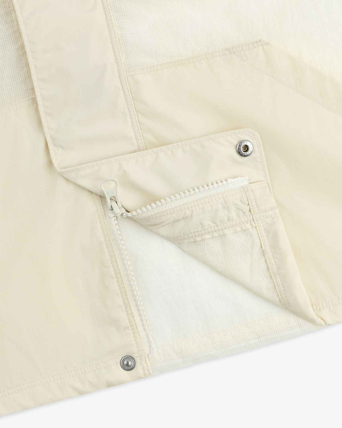 Close-up of a cream-colored Nylon Track Jacket featuring a zippered pocket and snap buttons.