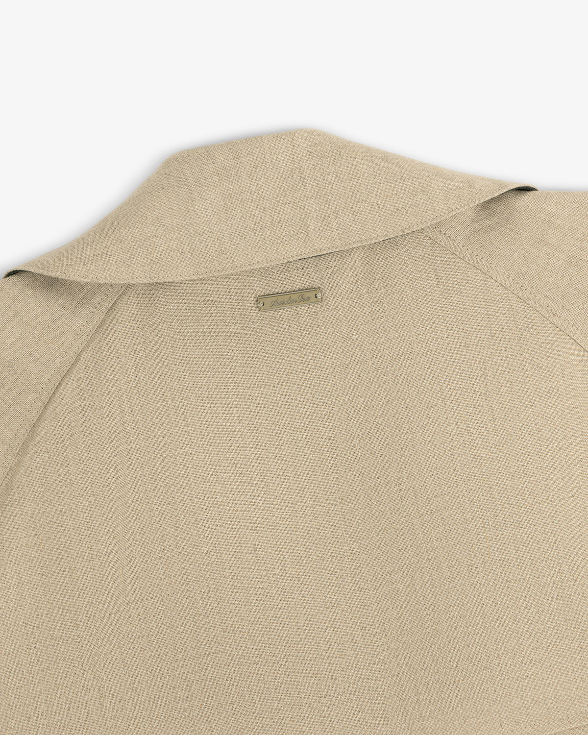 Close-up of the back collar and shoulder of the Linen Trench Coat in beige textured fabric with a small metal nameplate.