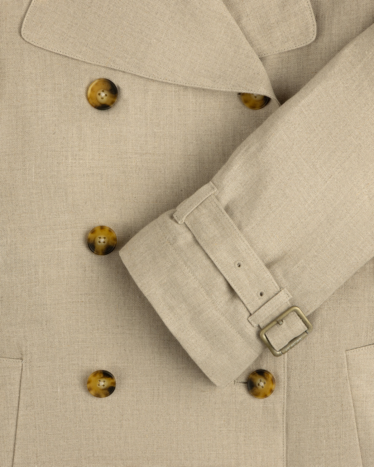 Close-up of Linen Trench Coat with brown buttons and belted cuff, highlighting the detailed fabric texture.