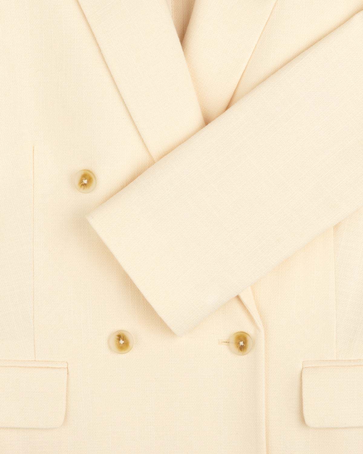 Close-up of the Double-Breasted Unconstructed Blazer in cream with four tan buttons, two front pockets, and a folded sleeve.