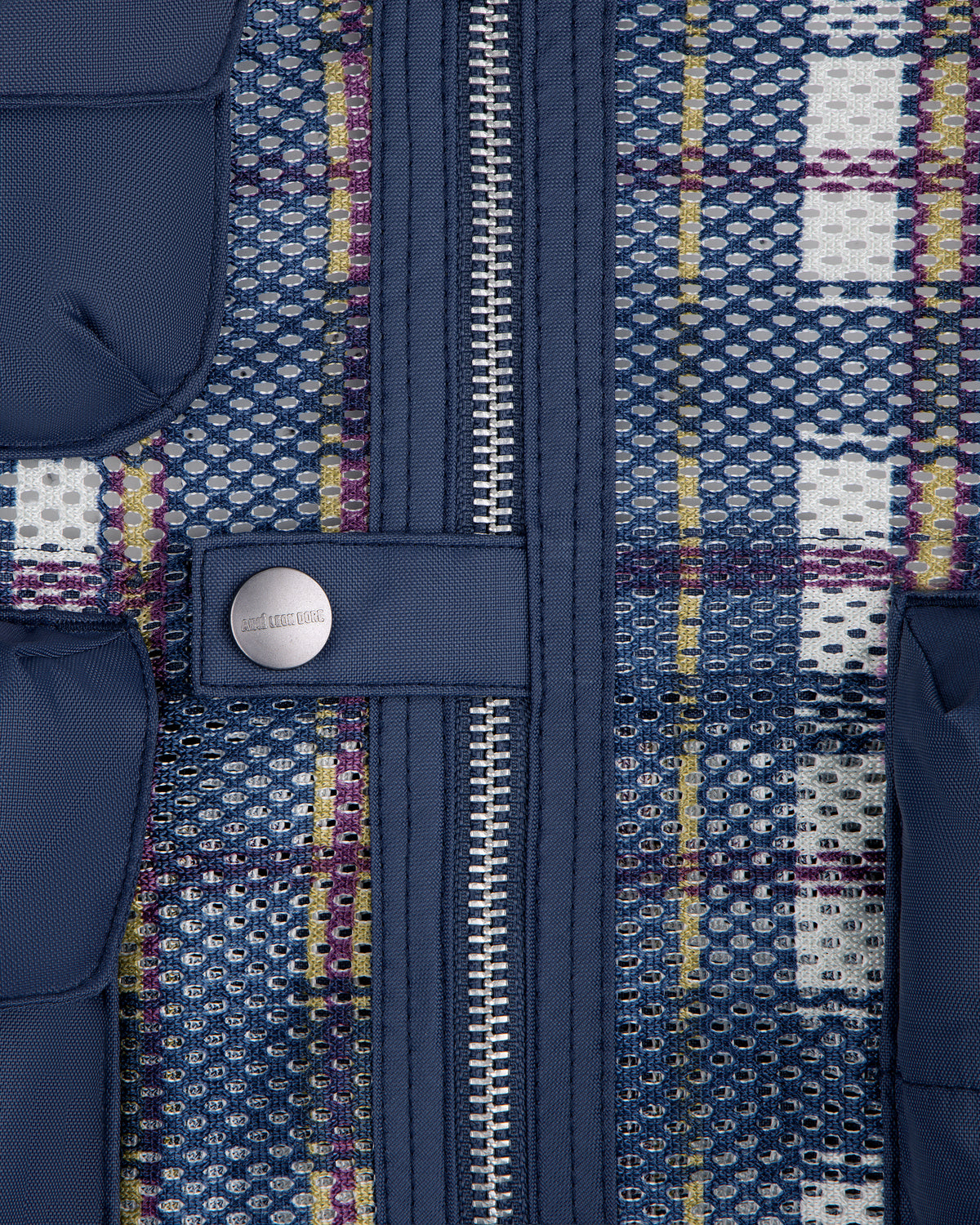 Close-up of blue zipper and snap button on Nylon Madras Utility Vest with multicolored grid and mesh pattern.