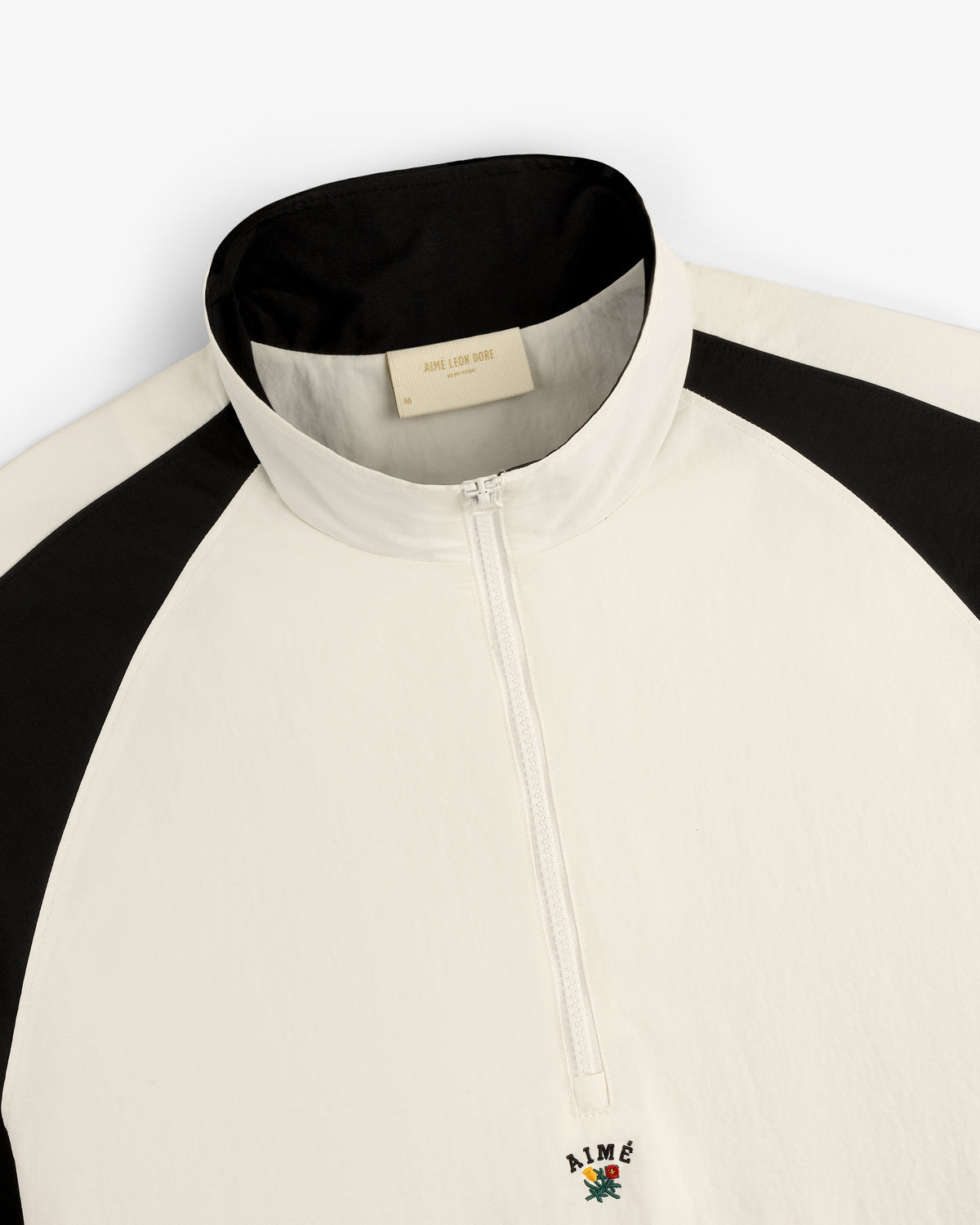 White and black Crest Nylon Half-Zip Pullover with stand collar and AIMÉ embroidered above a small colorful graphic.